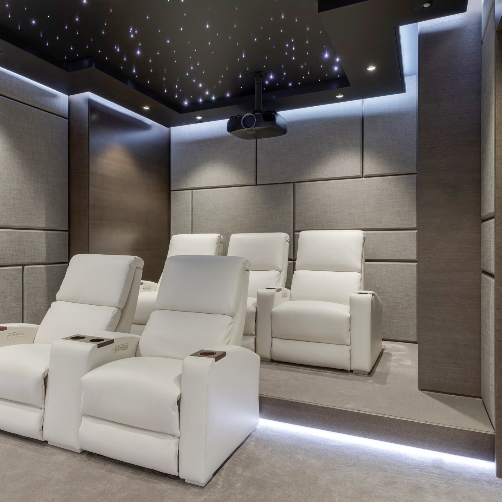 Pokój kina domowego z białymi fotelami rozkładanymi, projektorem i gwiaździstym sufitem.