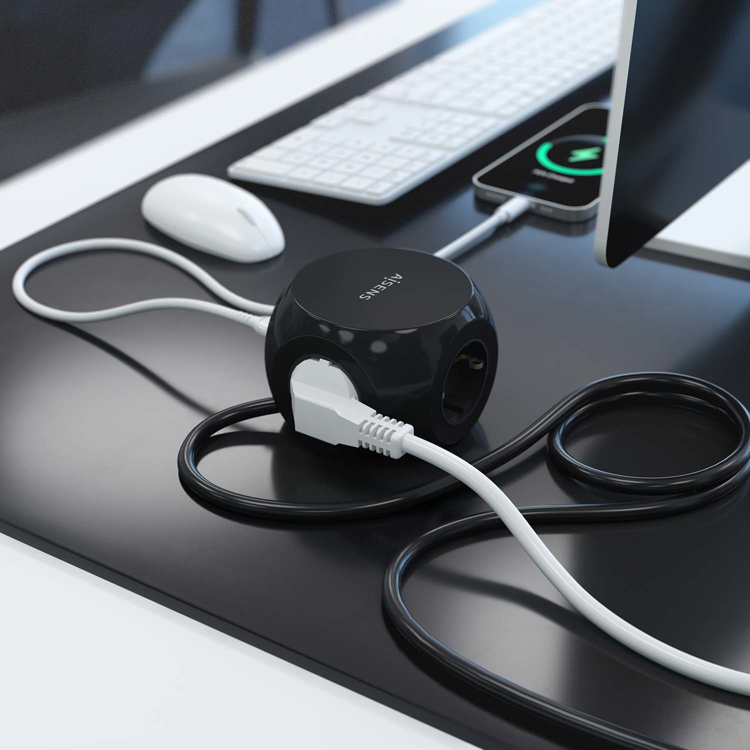 Un cubo di alimentazione nero su una scrivania con un computer e un telefono in carica.