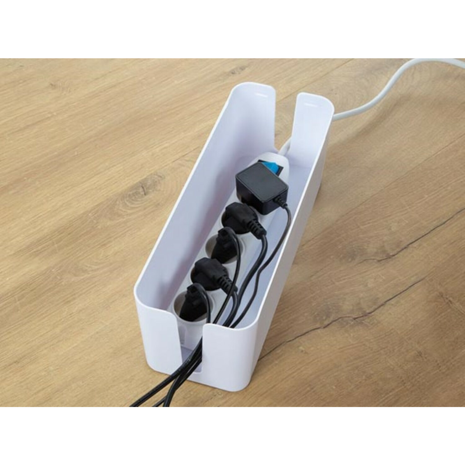 Biały organizer kablowy z kilkoma czarnymi przewodami zasilającymi i wtyczkami w środku, na jasnej drewnianej powierzchni.