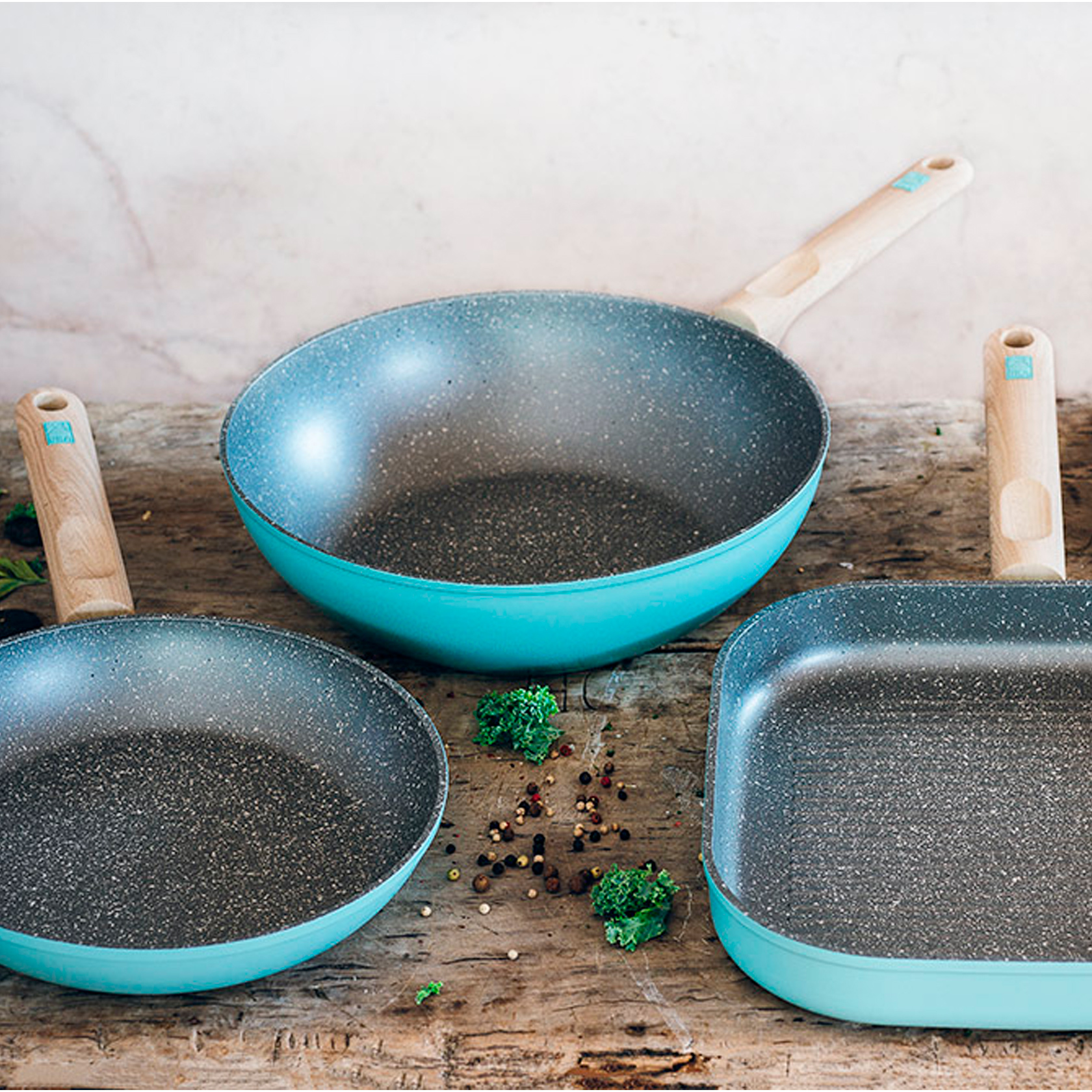 Zestaw trzech turkusowych patelni na drewnianej powierzchni.