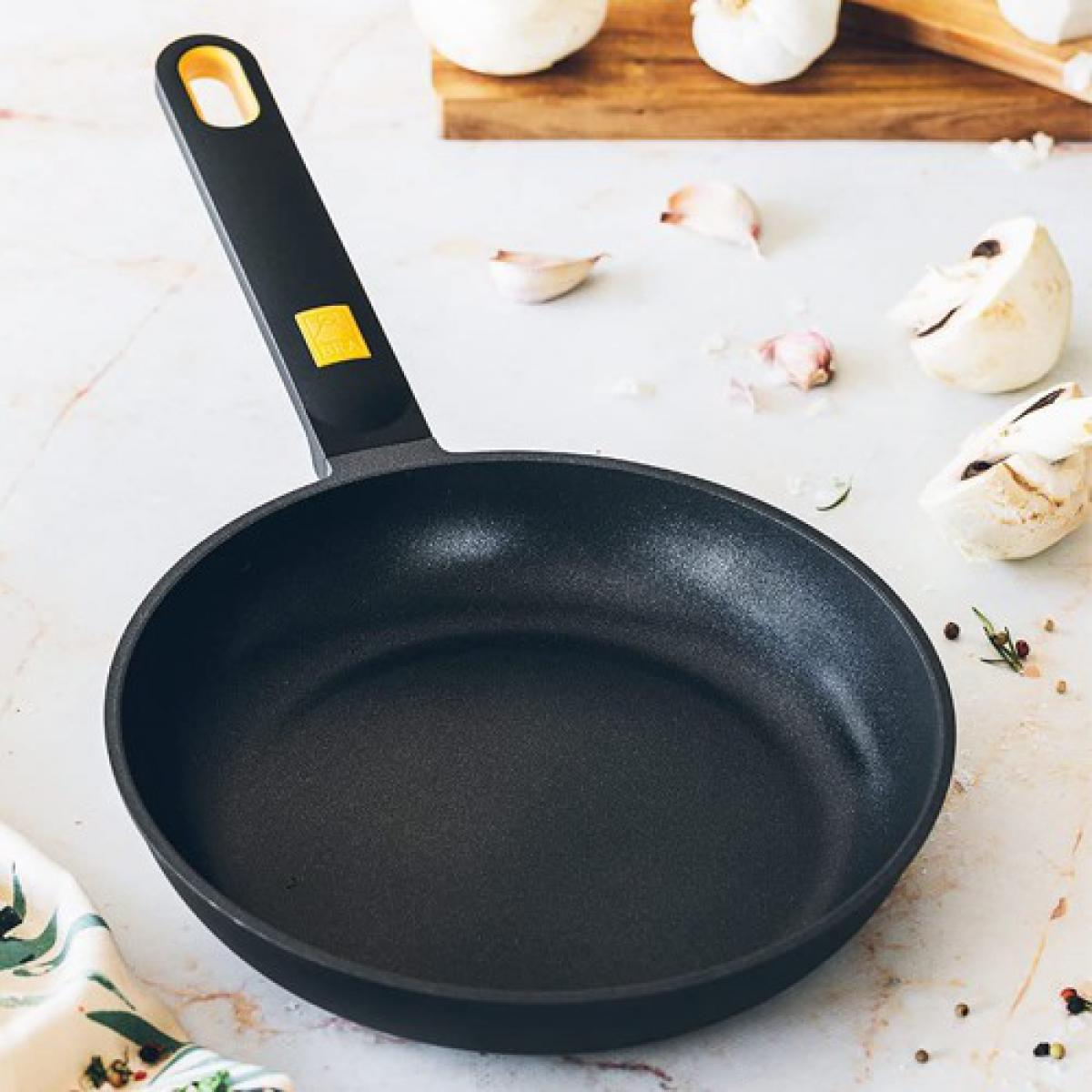 Czarna patelnia na marmurowej powierzchni z pieczarkami, czosnkiem i ziołami.