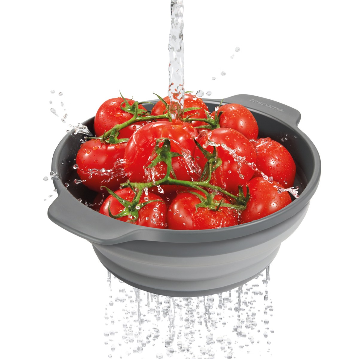 Rote Tomaten an Ranken werden in einem grauen Sieb gewaschen, Wasser spritzt auf sie.
