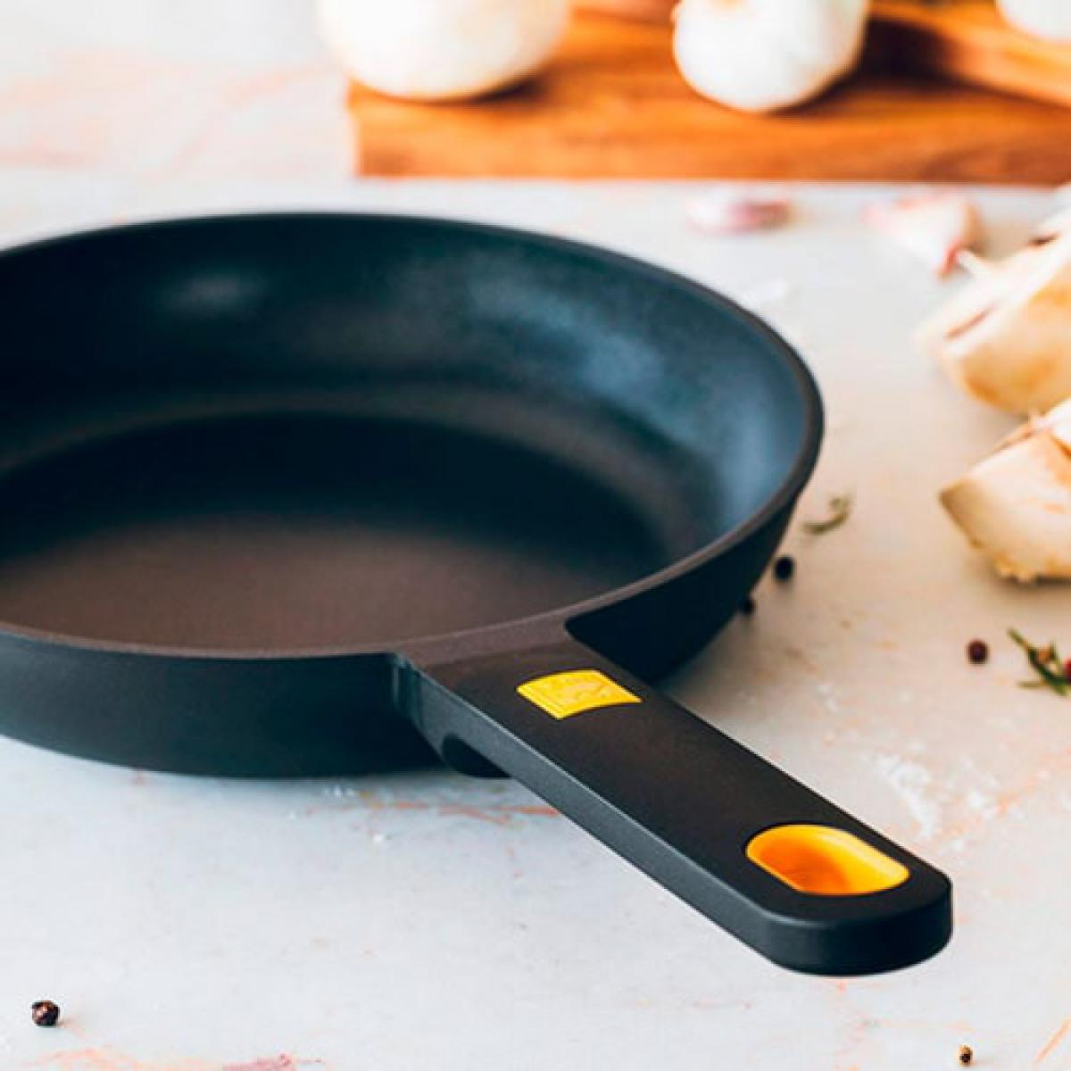 Sartén negro con mango, sobre una superficie con ajo y cebollas.
