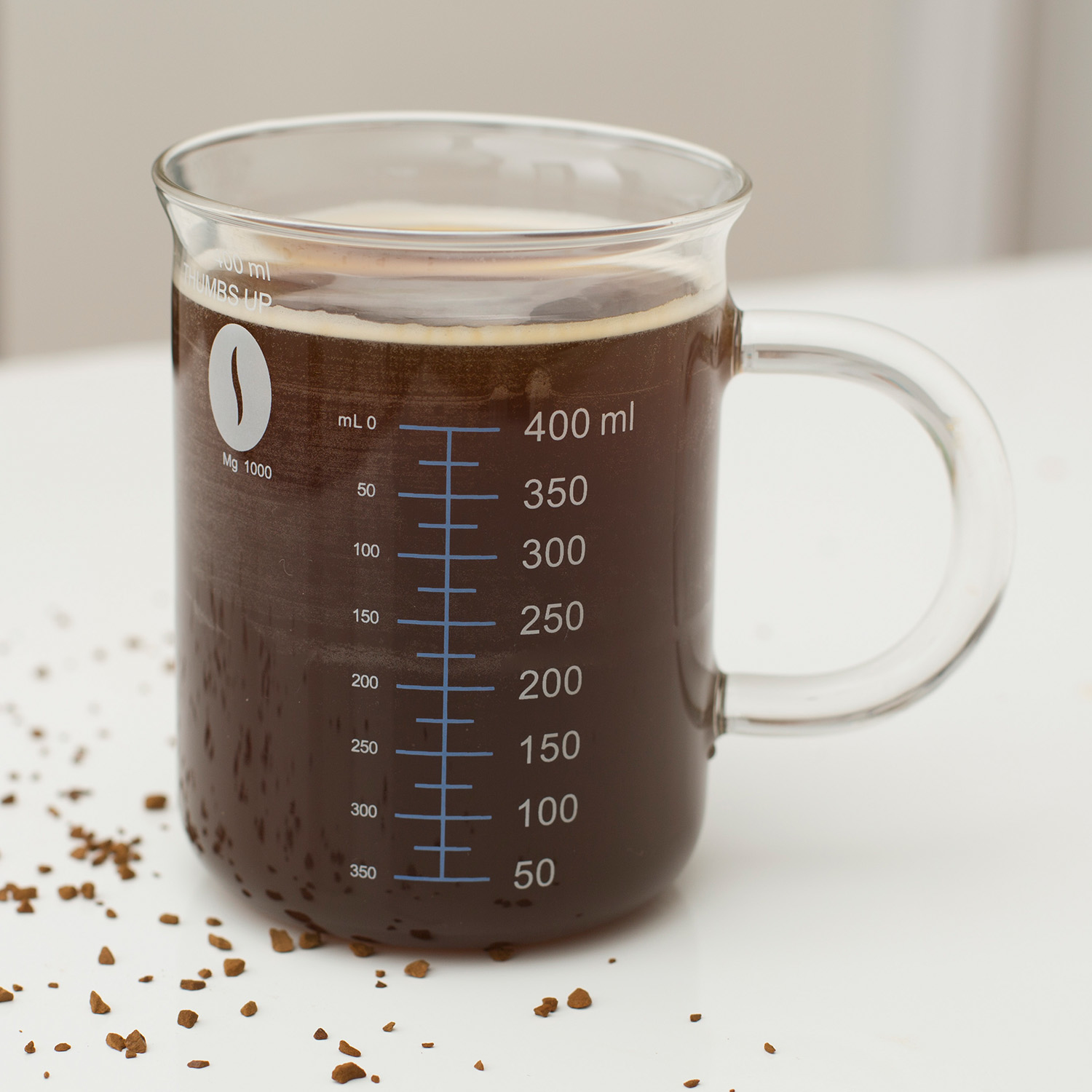 Szklany kubek z kawą, oznaczeniami i rozrzuconą kawą.