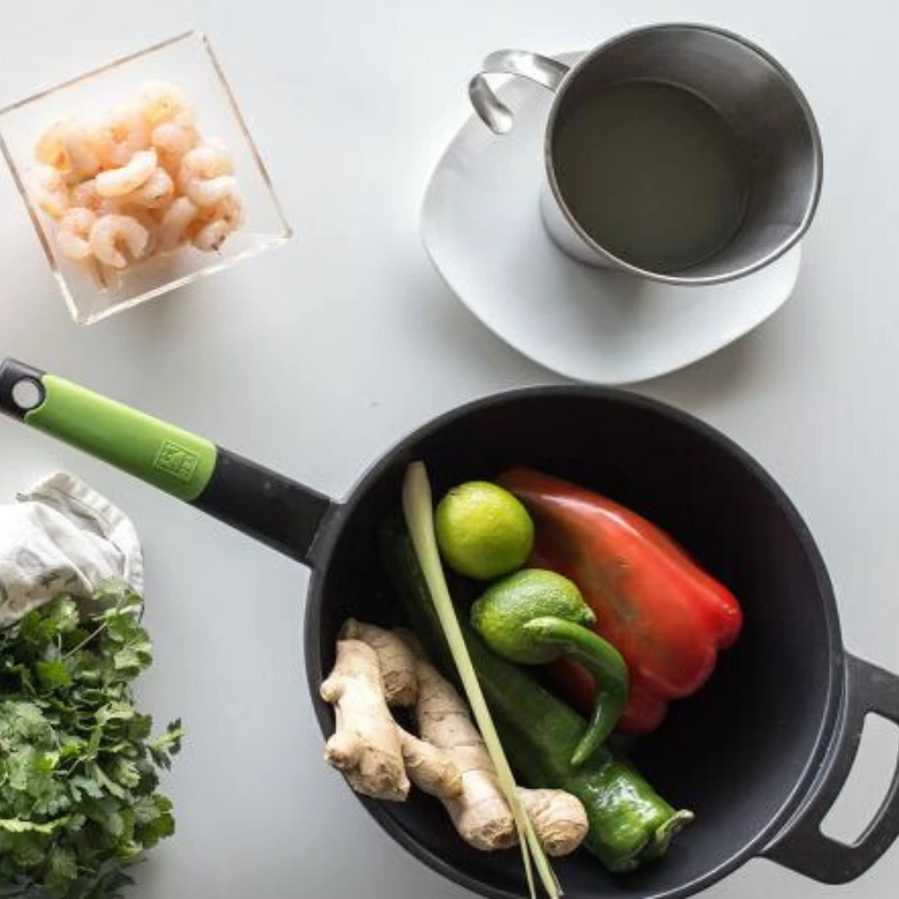 Patelnia wypełniona składnikami, takimi jak krewetki, cytryna i imbir na białym stole.