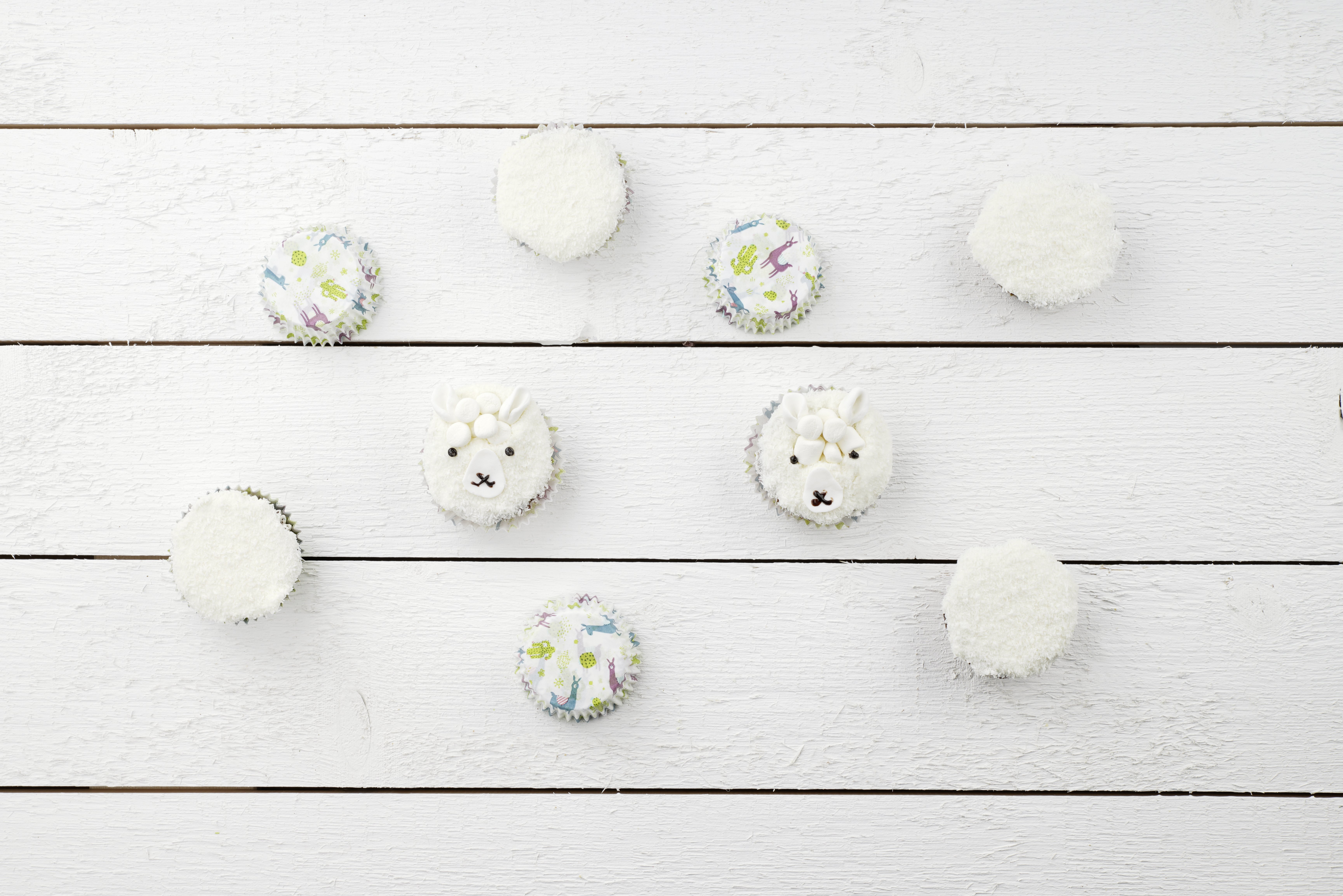 Cupcakes mit Lama-Gesichtern auf einer weißen Holzoberfläche.