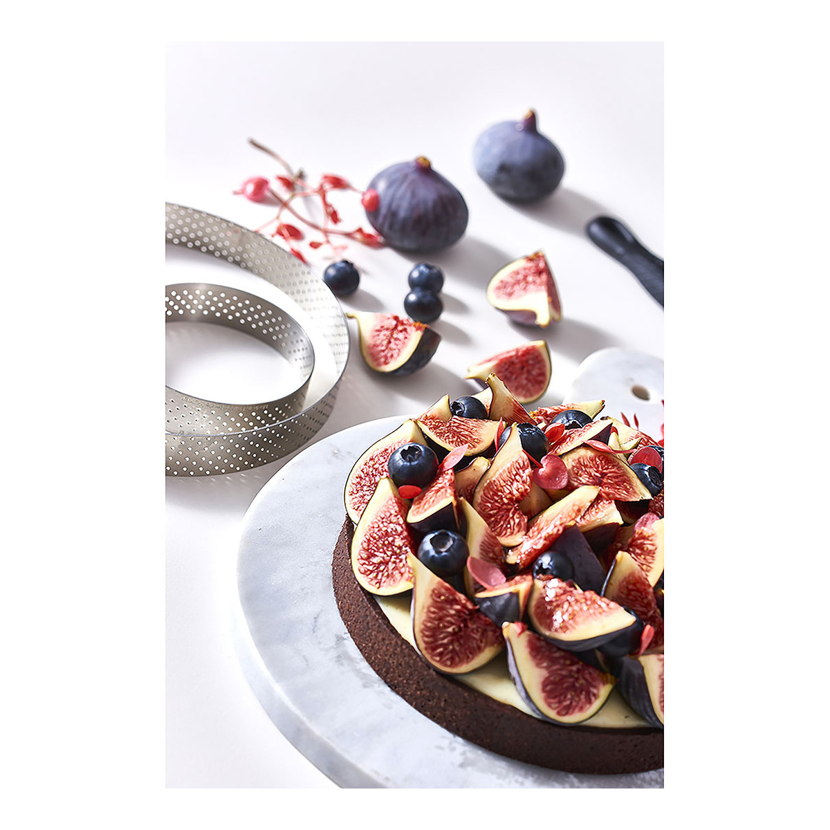 Ein Kuchen mit Feigen, Blaubeeren und einem Tortenring auf Marmor.