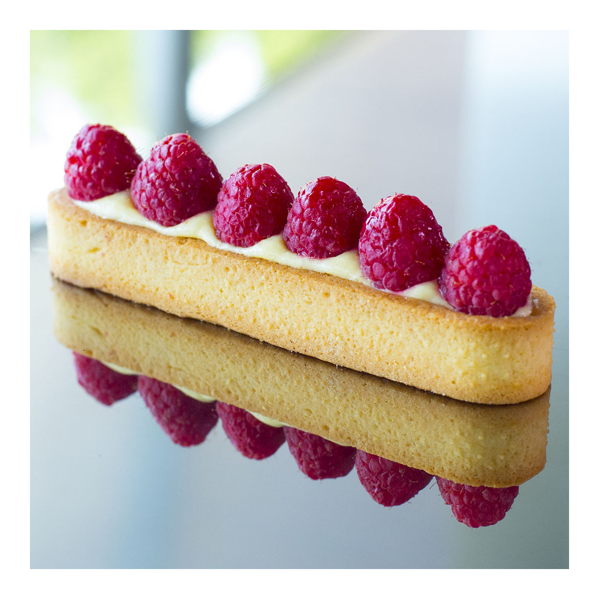 Dessert mit Himbeeren auf einer gespiegelten Oberfläche, mit weißem Hintergrund.