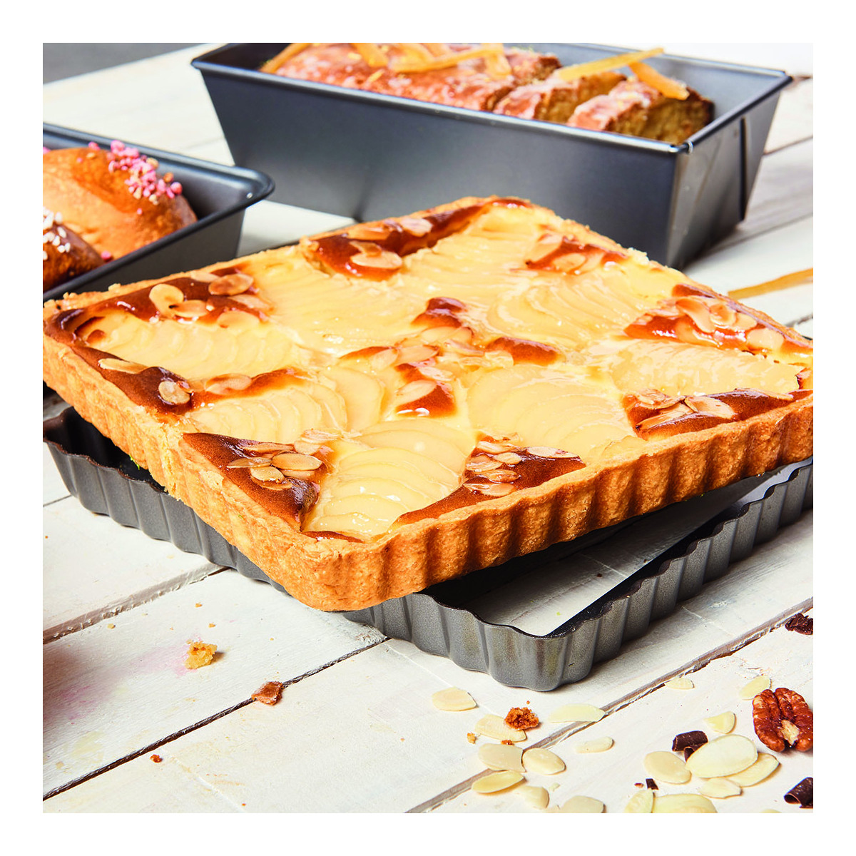 Pieczona tarta ze plastrami gruszek i migdałami. Na drewnianym stole, z innymi wypiekami i orzechami.