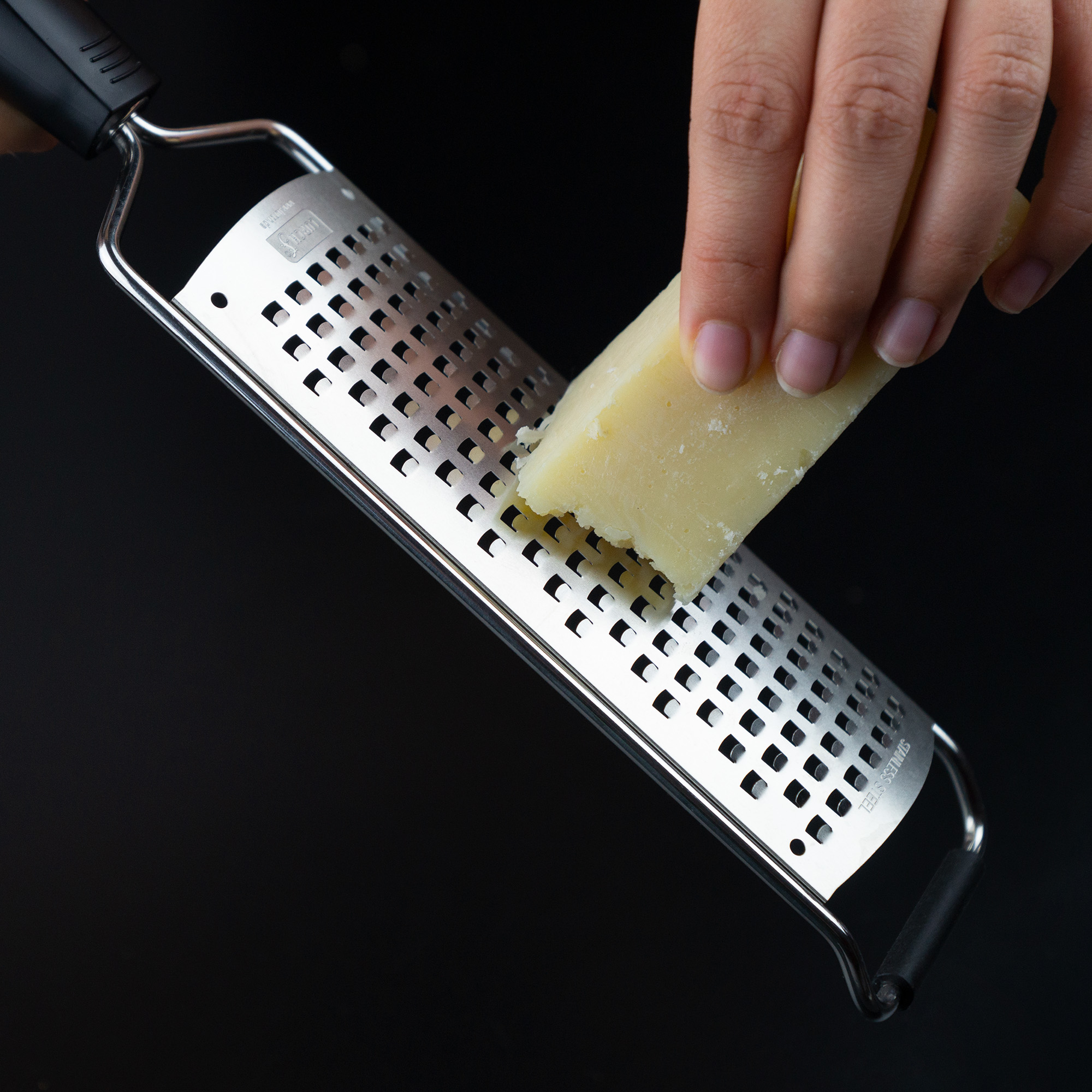 Handkäse auf einer Reibe mit schwarzem Griff auf dunklem Hintergrund reiben.