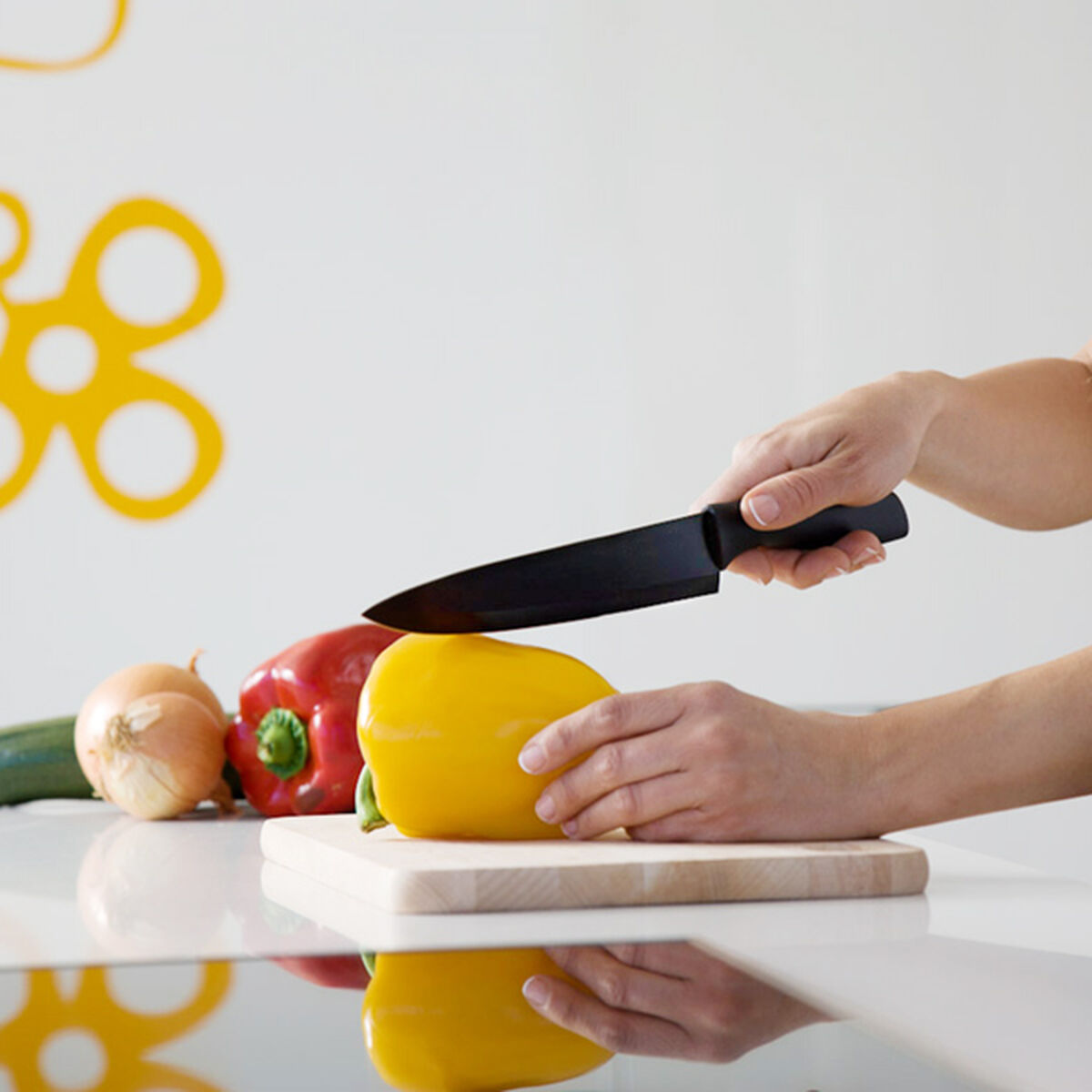 Osoba kroi żółtą paprykę czarnym nożem na desce do krojenia.