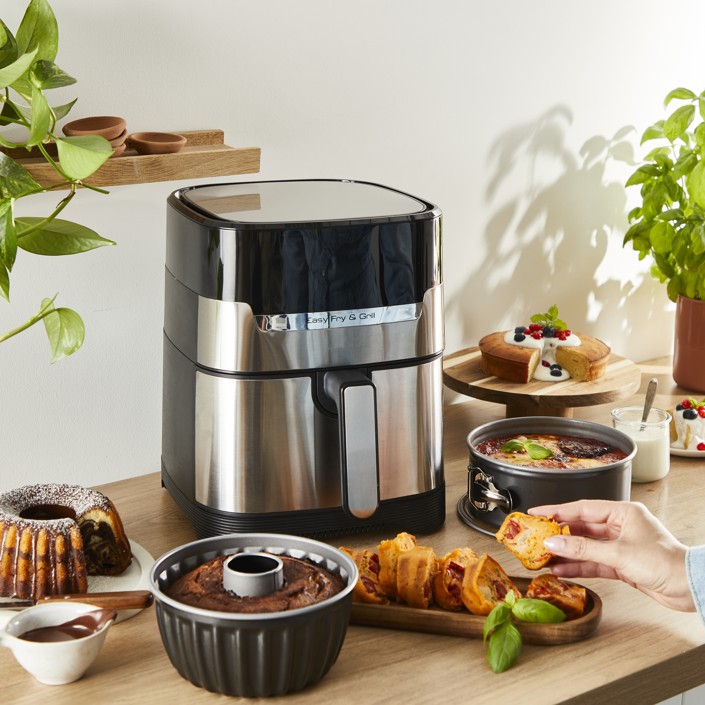 Frytownica powietrzna z produktami spożywczymi. Ciasta i inne produkty. Drewniany stół. Biała ściana.