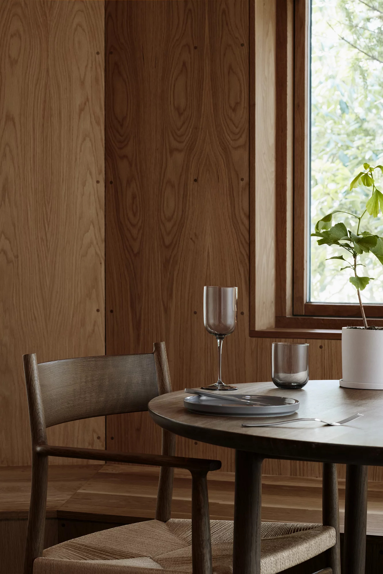 Holztisch für das Abendessen mit einem Stuhl und einem Fenster im Hintergrund. Hell und luftig.