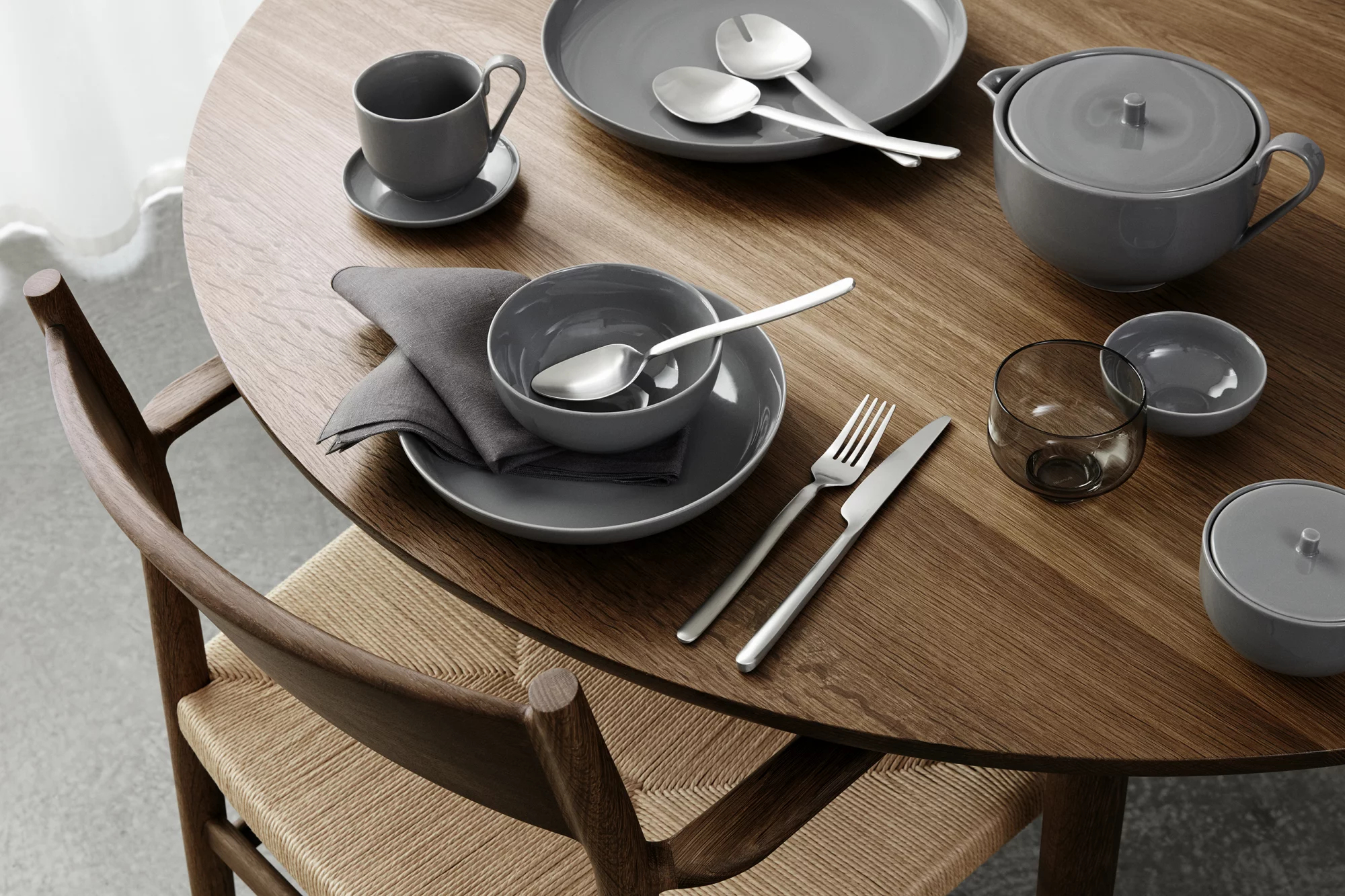 Tisch mit rundem Holztisch, Tellern, Besteck, einer Tasse und einer Schüssel. Natürliches Licht.