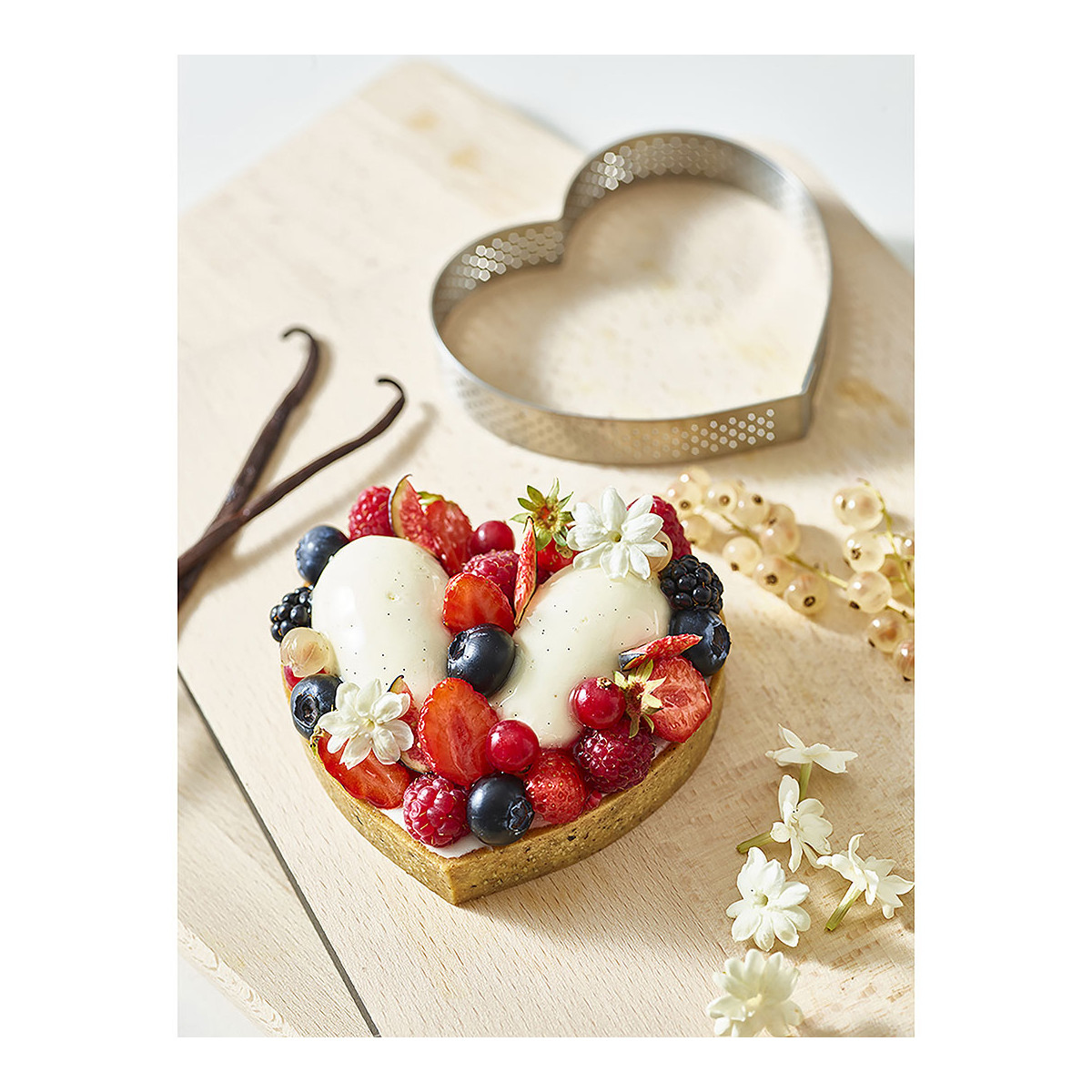 Herzförmige Tarte mit Früchten und Blumen auf Holzbrett, Vanilleschoten.