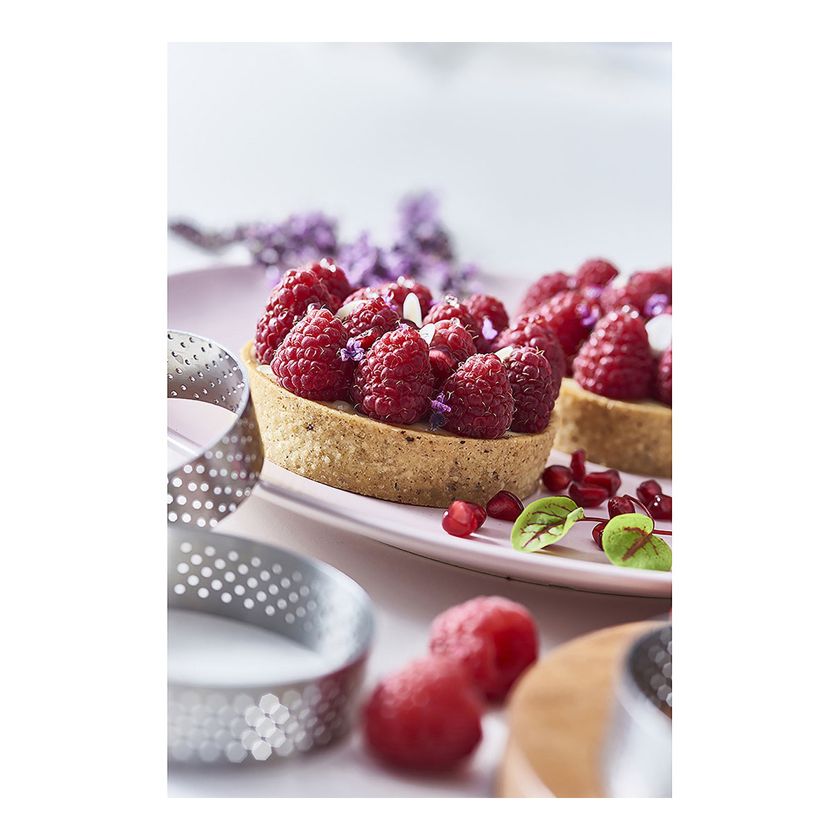 Deux mini-tartes aux framboises sur une assiette rose, avec framboises et anneaux épars.