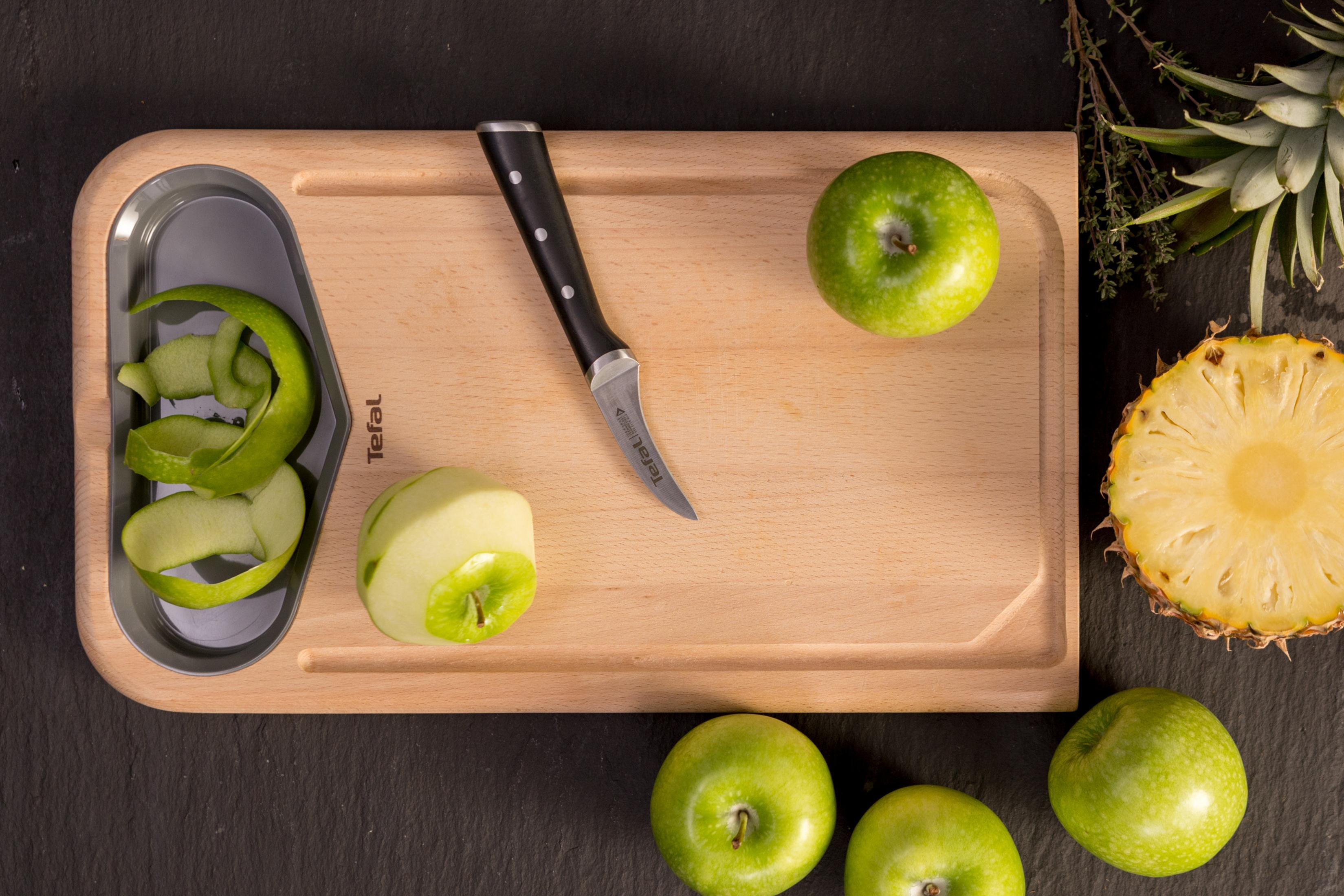 Drewniana deska do krojenia z zielonymi jabłkami, nożem i ananasem. Obierki.