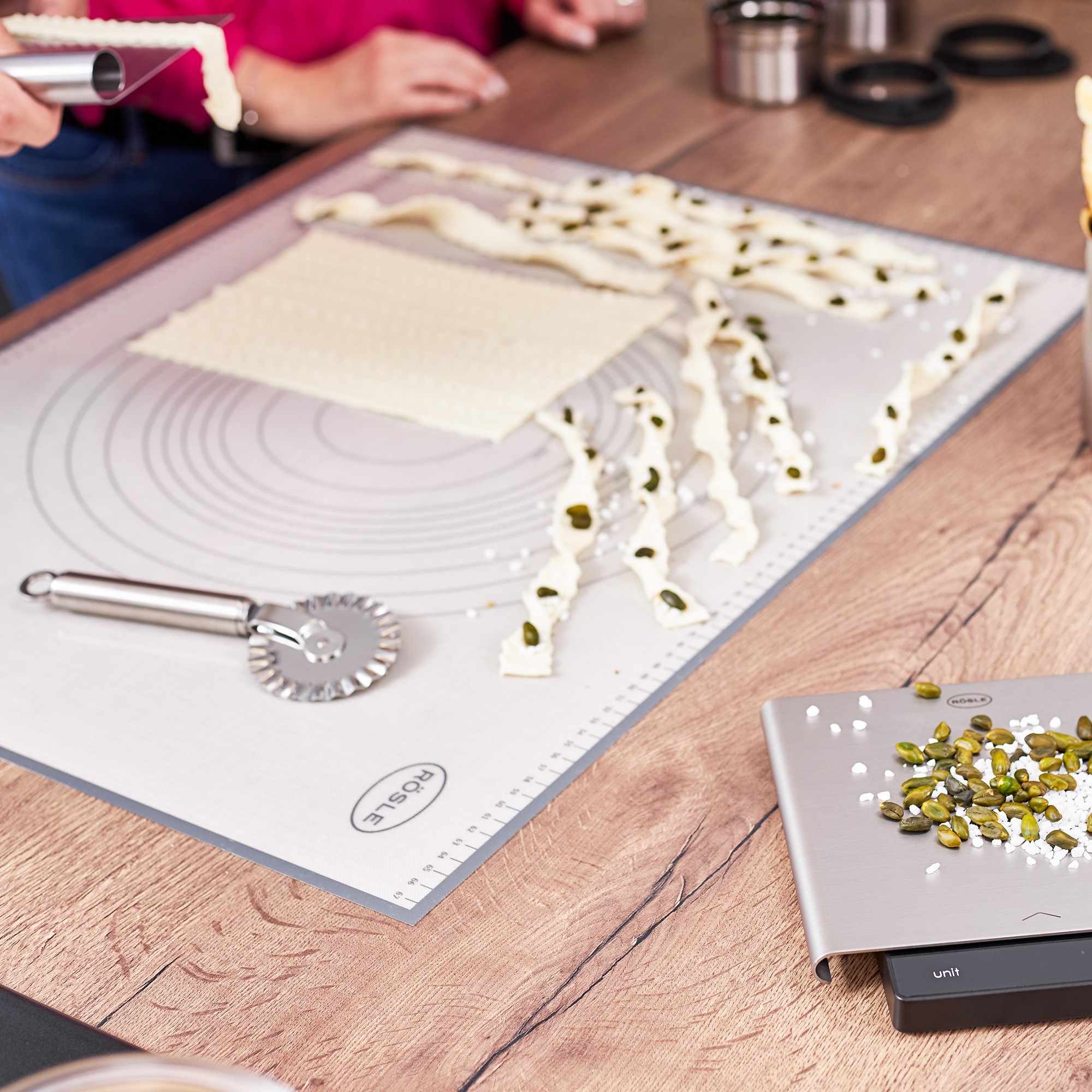 Ręce przygotowują ciasto z pestkami dyni na drewnianej powierzchni. Wałek, waga i inne narzędzia.