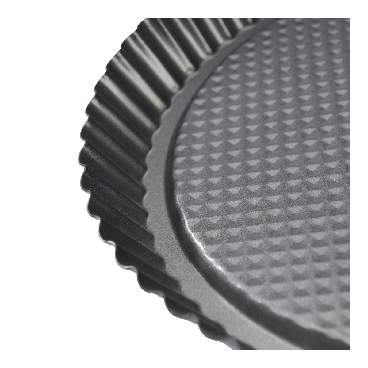 Zbliżenie na karbowaną formę do tarty, ze wzorzystą podstawą.