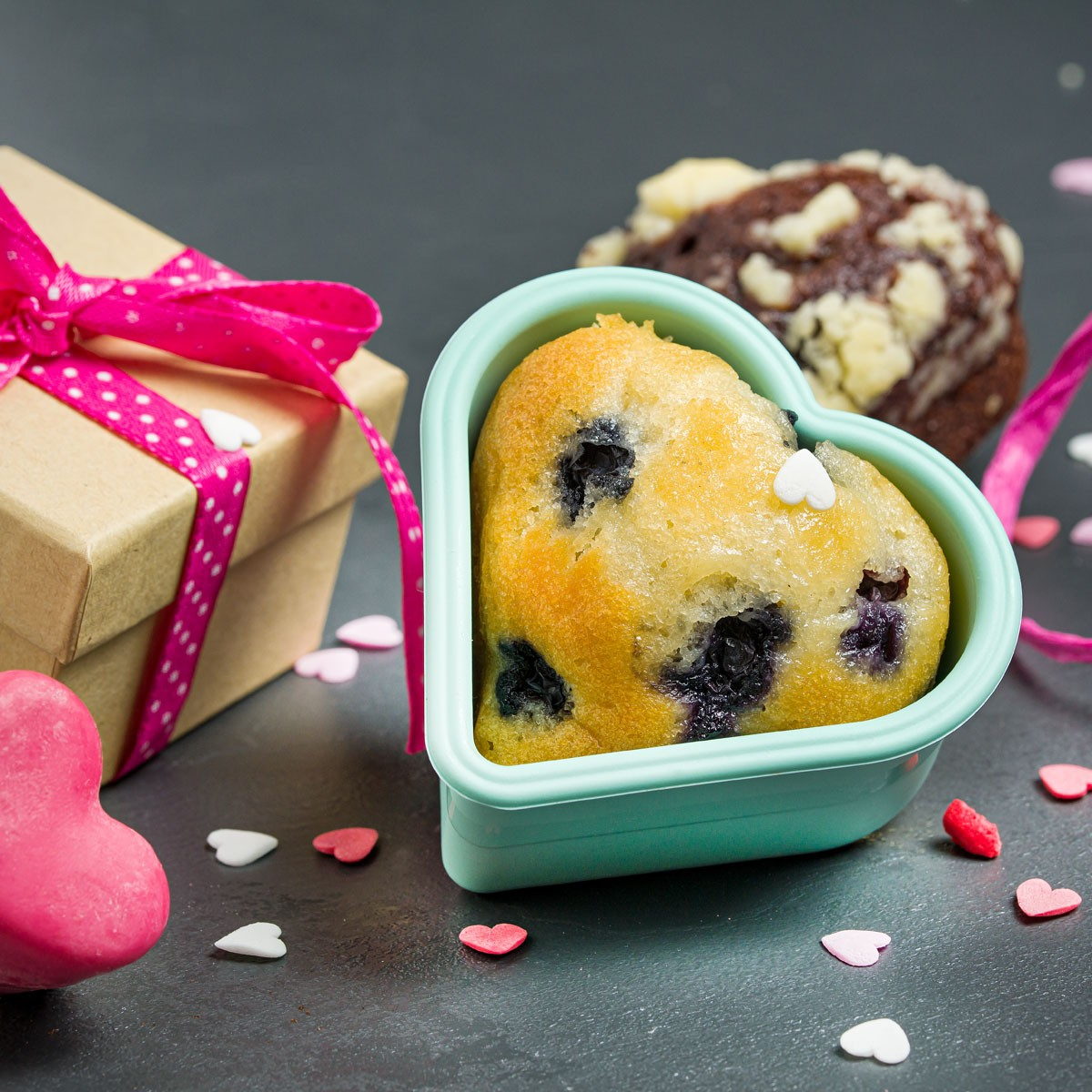 Herzförmige Muffins und Geschenkbox mit rosa Schleife. Dekorative Herzen. Dunkler Hintergrund.
