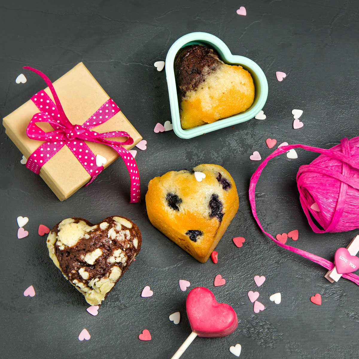 Herzförmige Muffins, Geschenkbox und dekorative Herzen auf schwarzer Oberfläche.