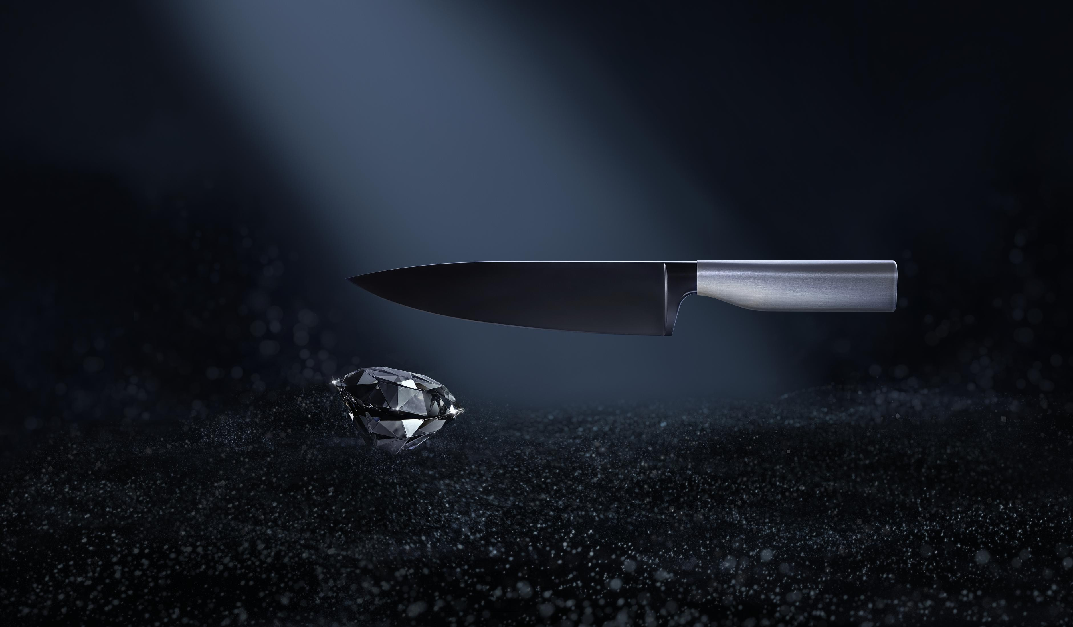 Schwarzes Messer liegt auf einem Diamanten, auf dunklem Hintergrund mit blauem Scheinwerfer.