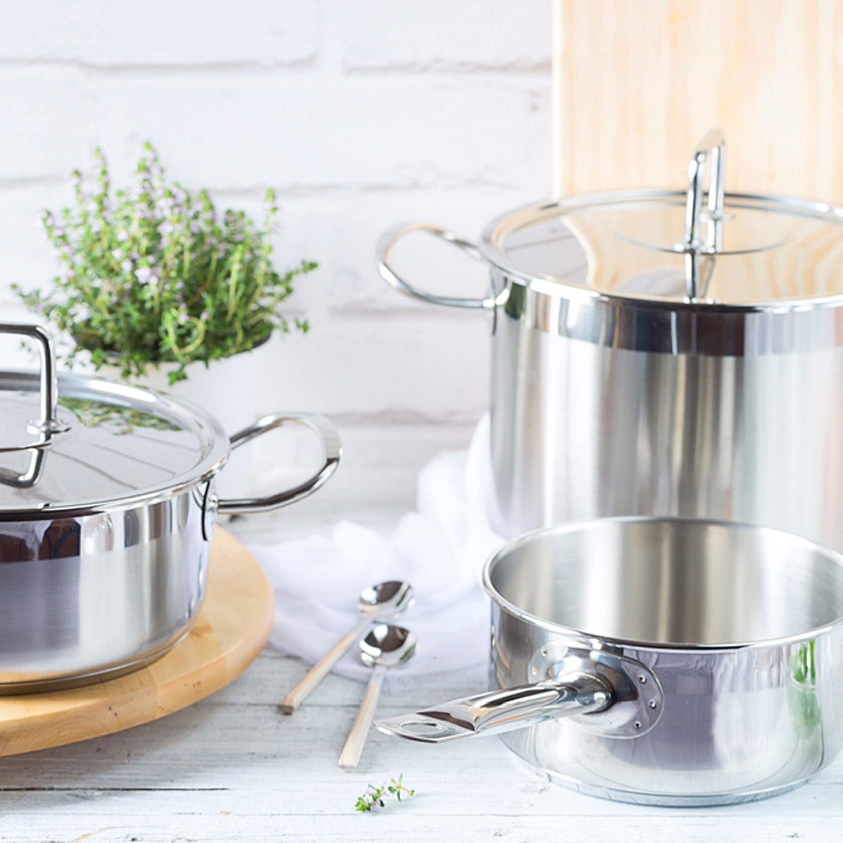 Garnki i pokrywki ze stali nierdzewnej z uchwytami na drewnianej powierzchni, białe tło.