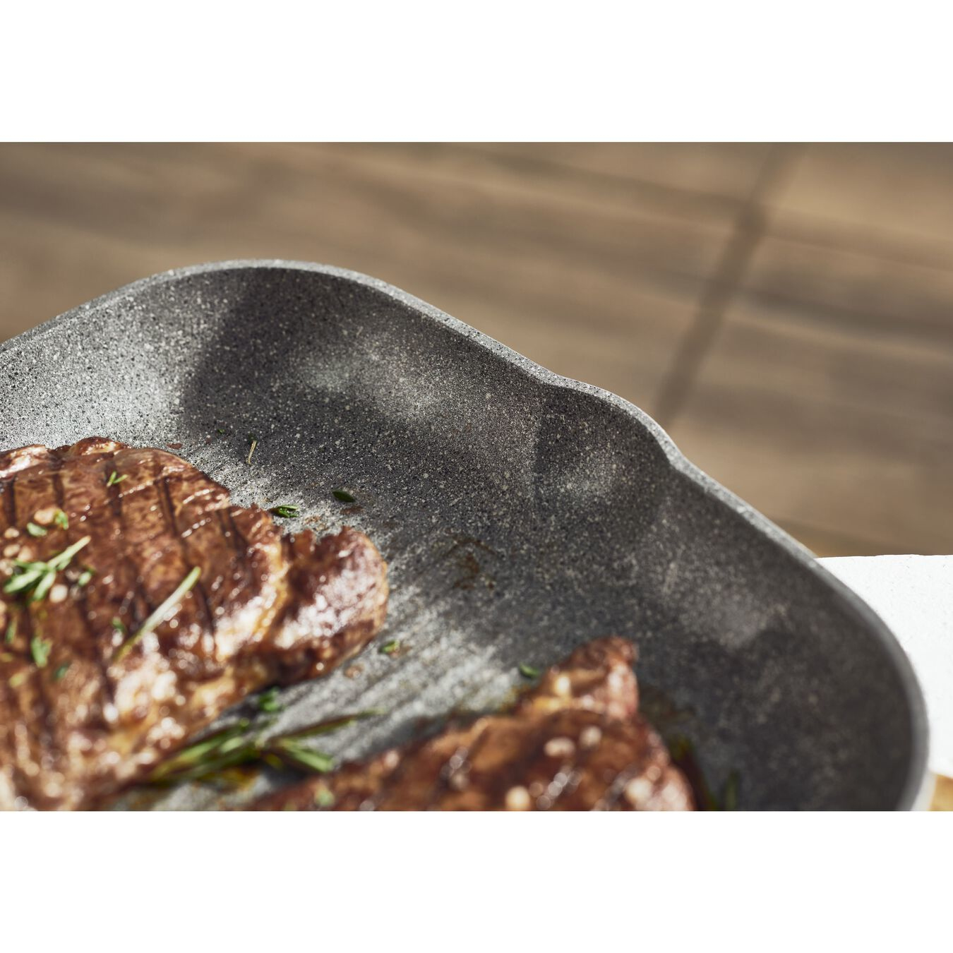 Nahaufnahme einer Grillpfanne mit gegrilltem Steak. Rosmaringarnierung sichtbar.