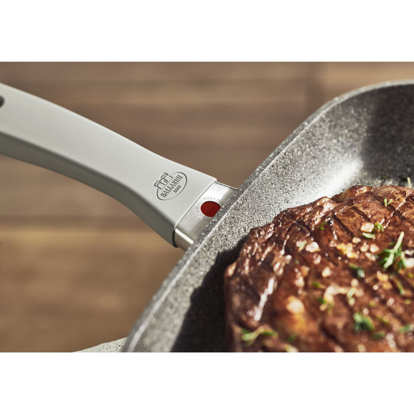Nahaufnahme eines Pfannengriffs und gegrilltem Steak. Holzoberfläche im Hintergrund.