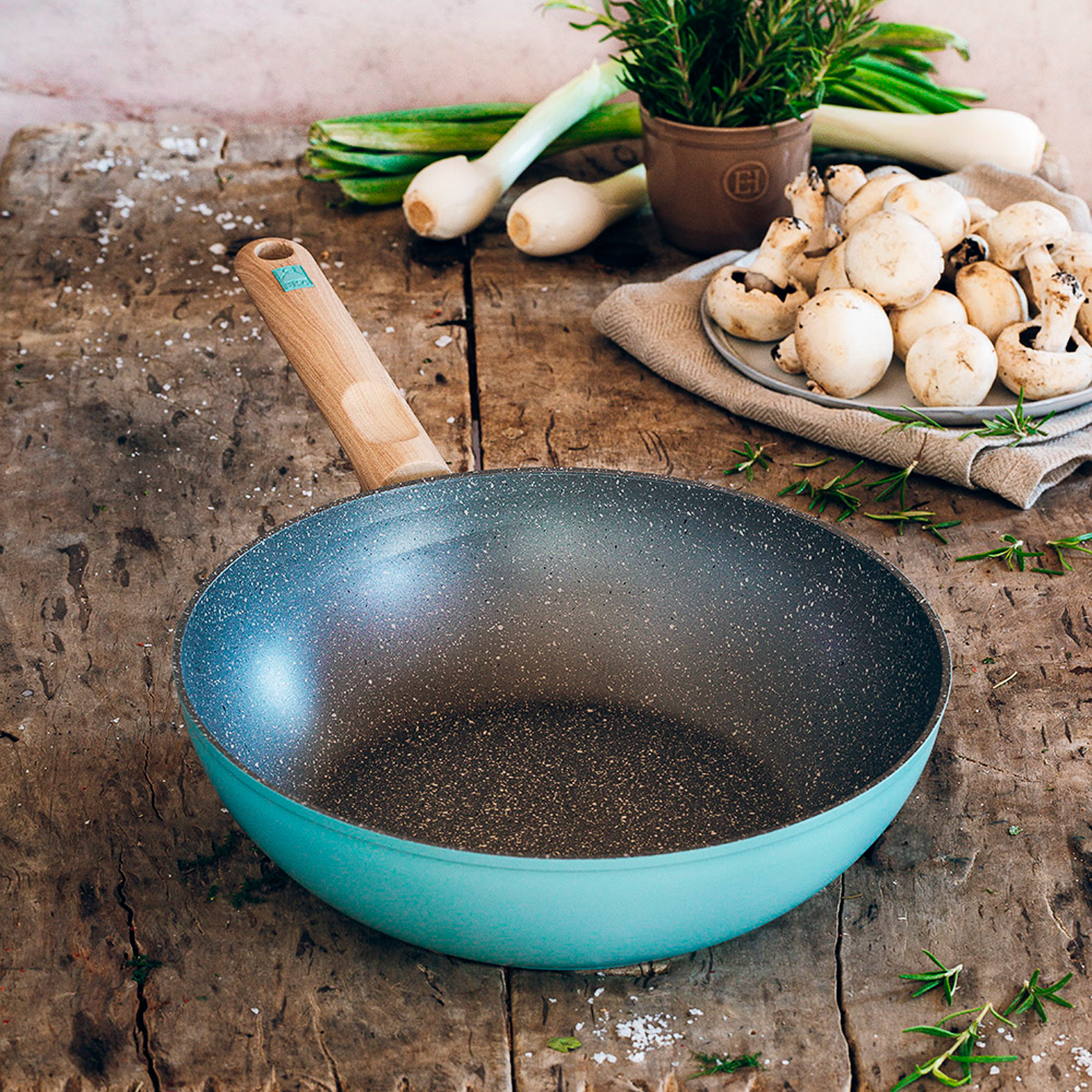 Niebieski wok z drewnianym uchwytem na drewnianym stole. Warzywa, takie jak por i grzyby w tle.