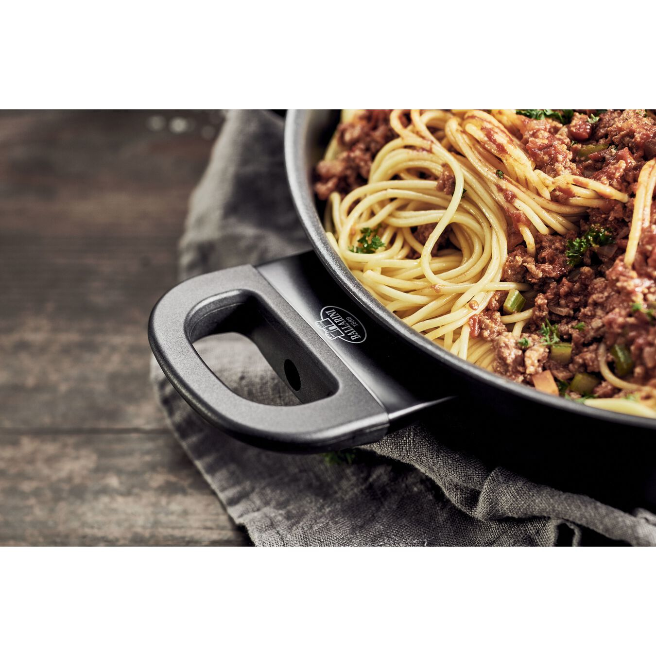 Patelnia spaghetti z sosem mięsnym, na drewnianym stole z szarą szmatką.