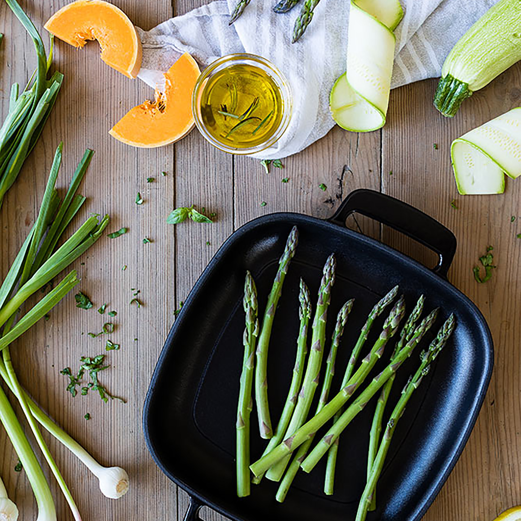 Draufsicht auf Spargel in der Pfanne mit Gemüse und Öl auf einem Holztisch.
