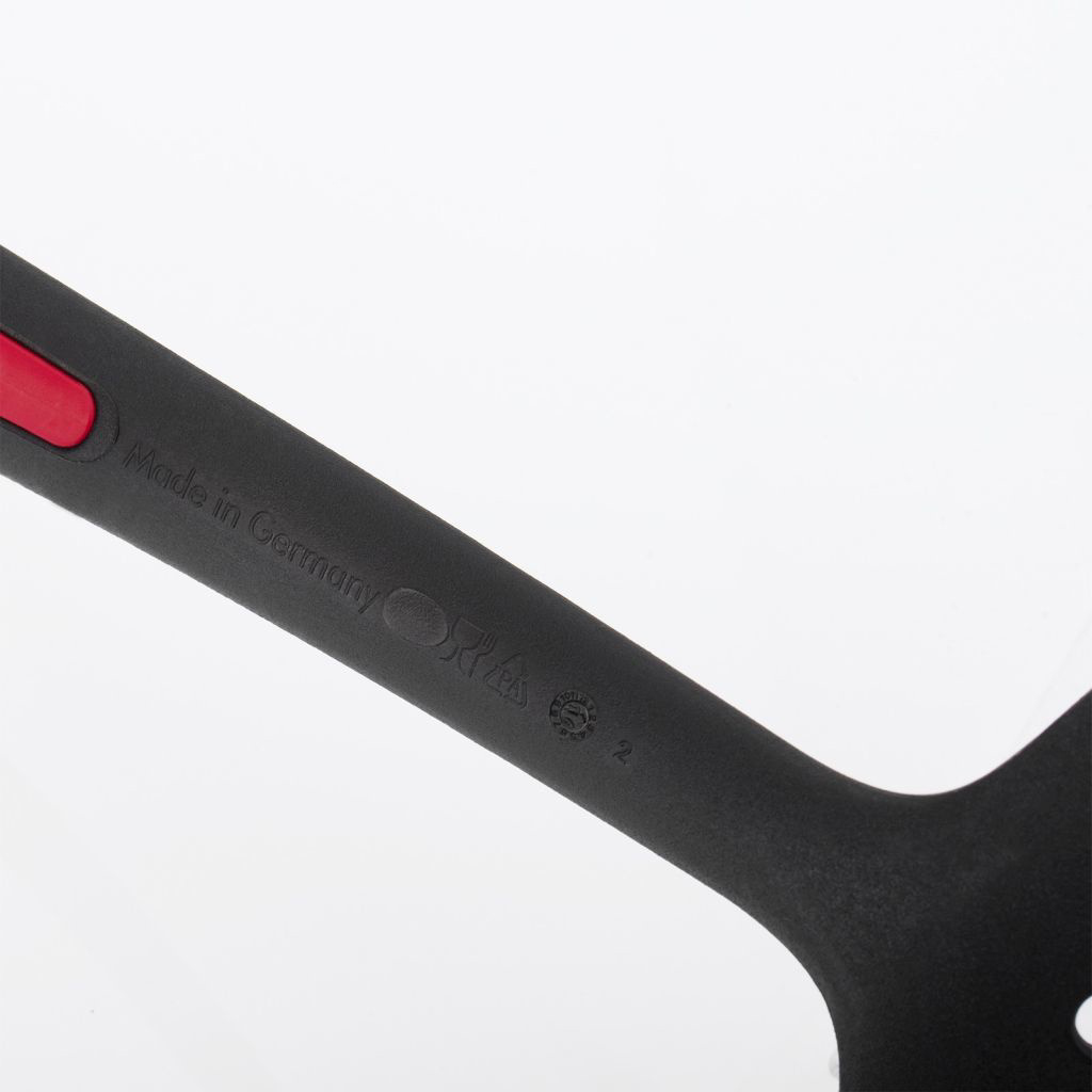 Primo piano del manico di un cucchiaio forato nero. Testo Made in Germany. Sfondo bianco.
