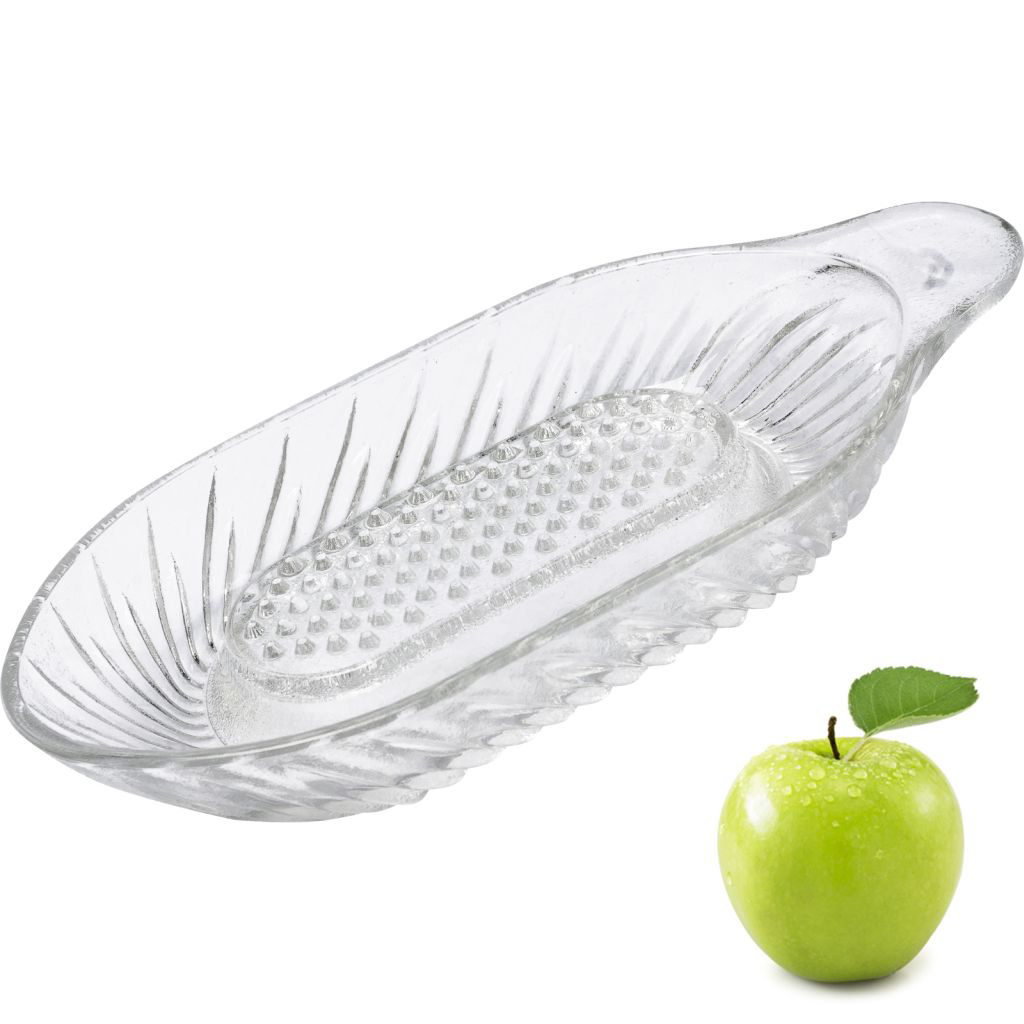 Eine durchsichtige Glasservierschale mit einem grünen Apfel daneben. Die Schale ist leer.