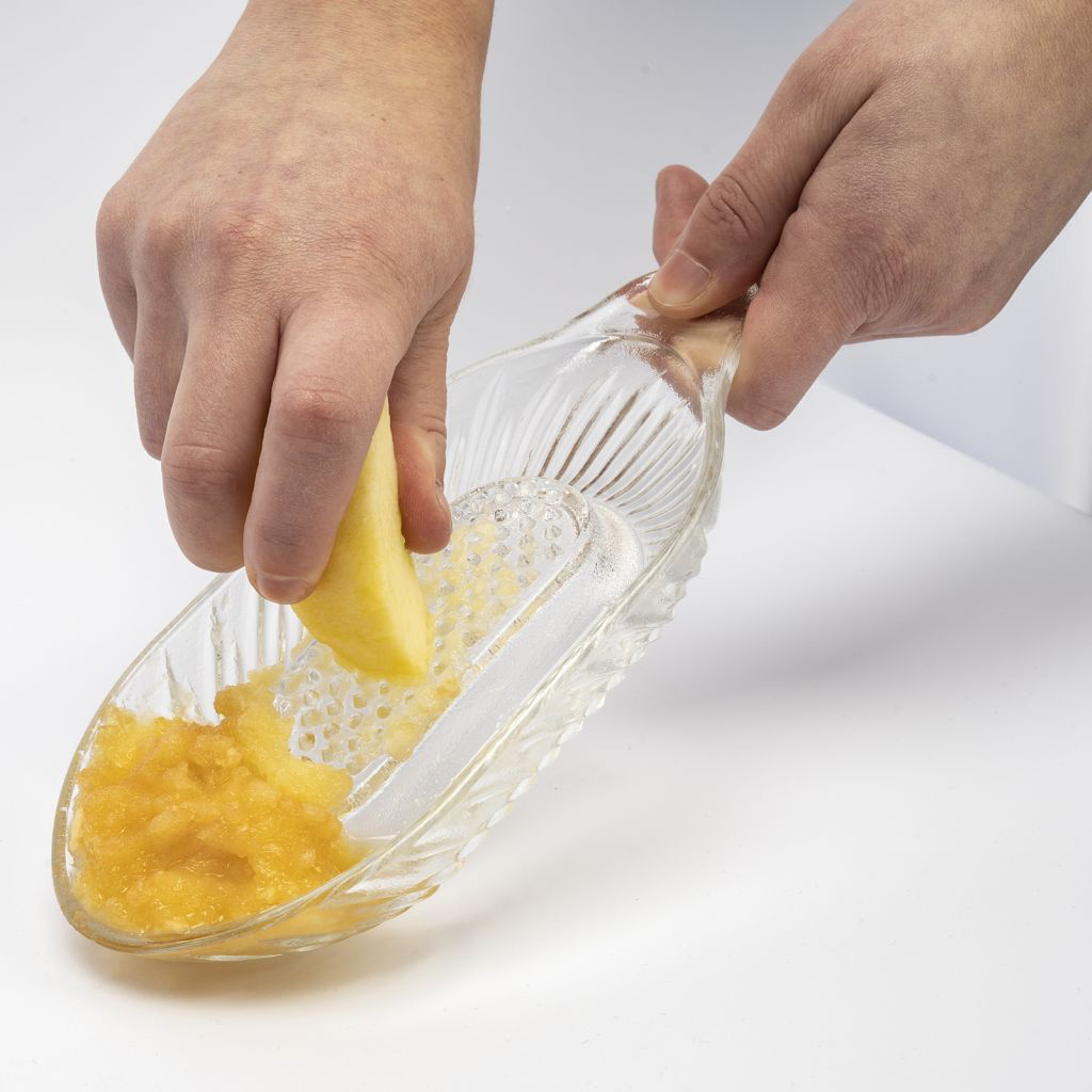 Hände, die einen Apfel in einen Glasreibe raspeln. Geriebener Apfel ist im Glas.