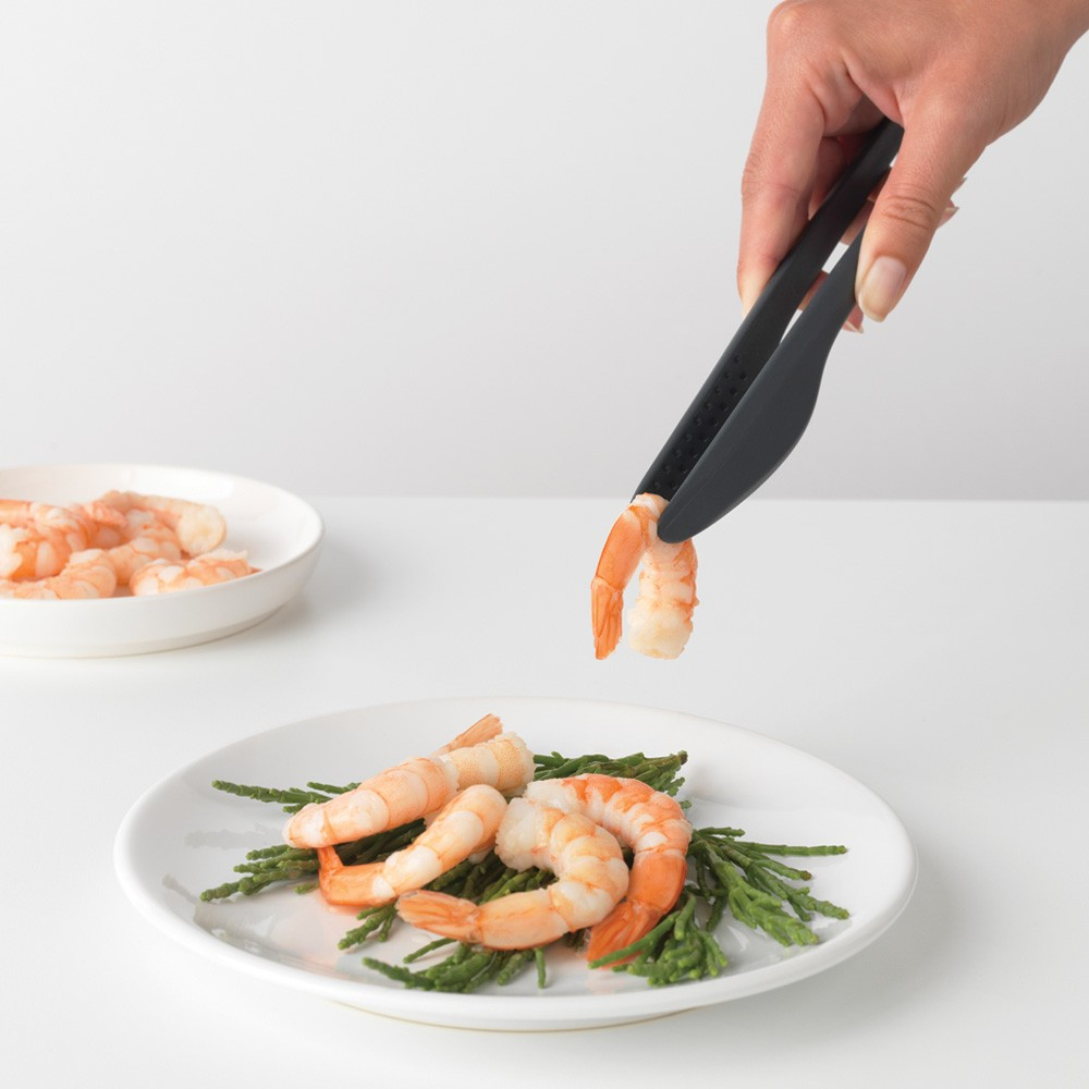 Una mano usa delle pinze per mettere un gamberetto su un piatto con altri gamberetti e verdure.