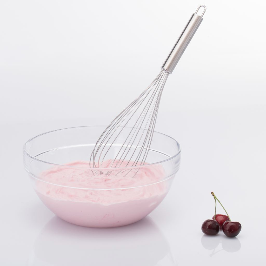 Schneebesen in einer Glasschüssel mit rosa Mischung und drei Kirschen auf weißer Oberfläche.