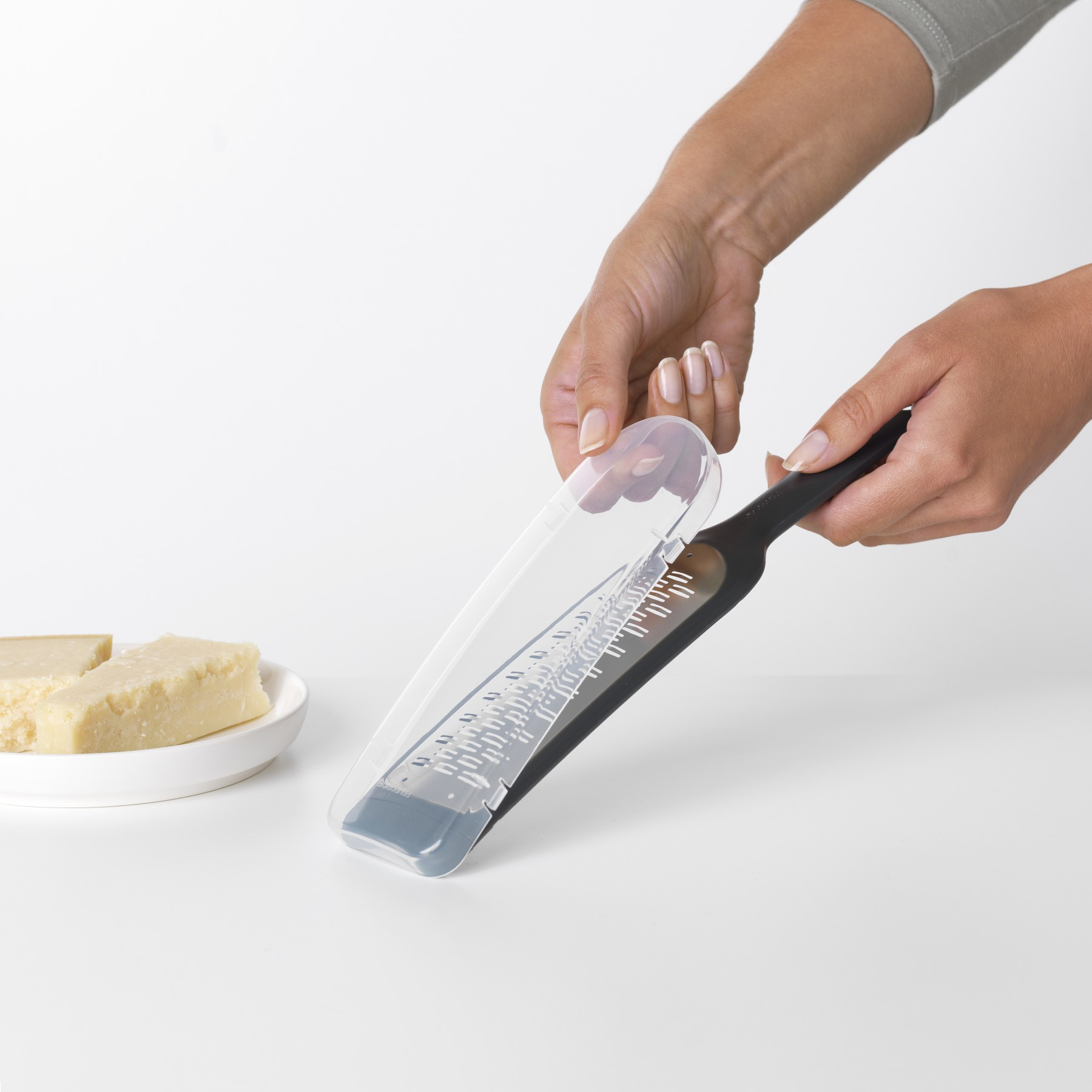 Hände, die Käse über einen Teller reiben. Parmesan-Käse. Weißer Hintergrund.