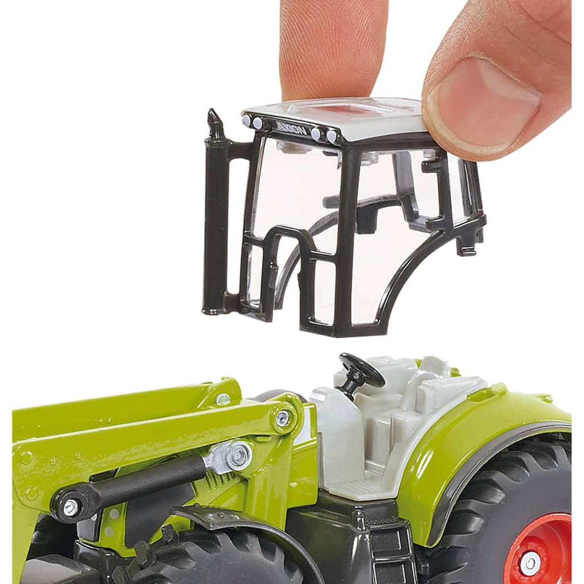 Eine Hand hält eine Traktorkabine. Der Traktor ist grün und weiß. Die Kabine ist schwarz und weiß.