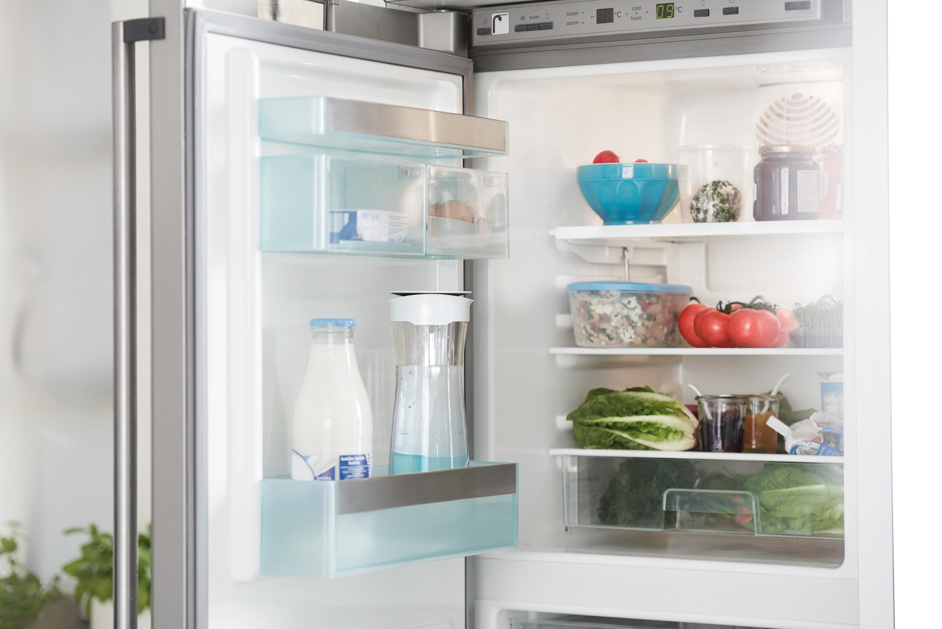 Kühlschrank geöffnet mit Essen. Milch, Gemüse und andere Gegenstände sind sichtbar. Helles Licht.