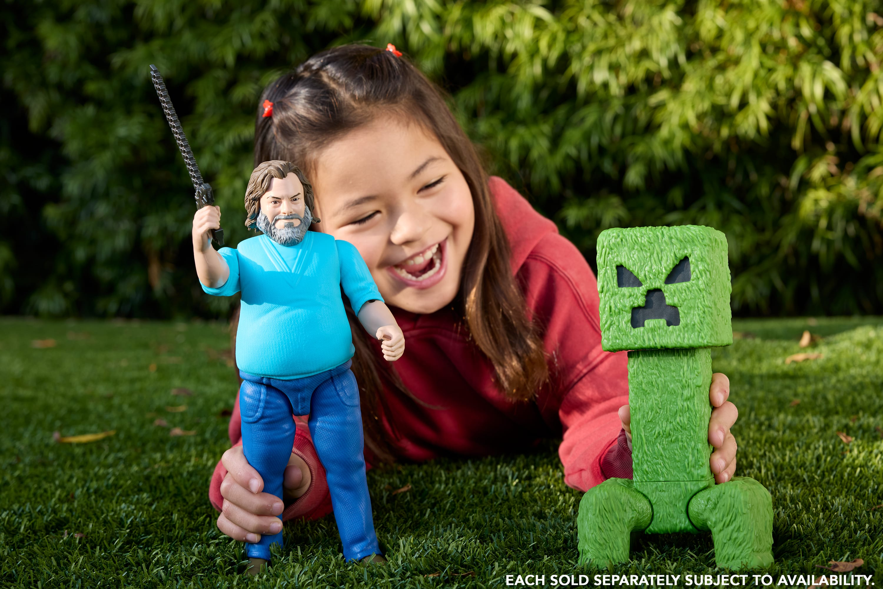 Una niña y figuras de Minecraft sobre hierba. La niña sonríe, sosteniendo juguetes de Steve y Creeper.