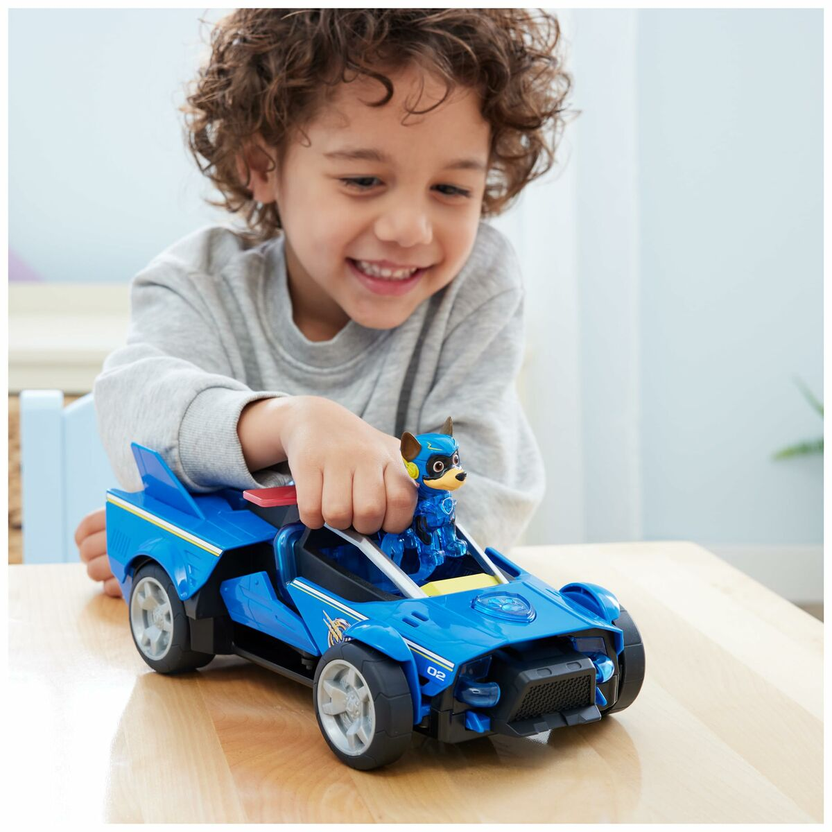 Un niño pequeño jugando con un coche de juguete azul con una figura de perro en una mesa.
