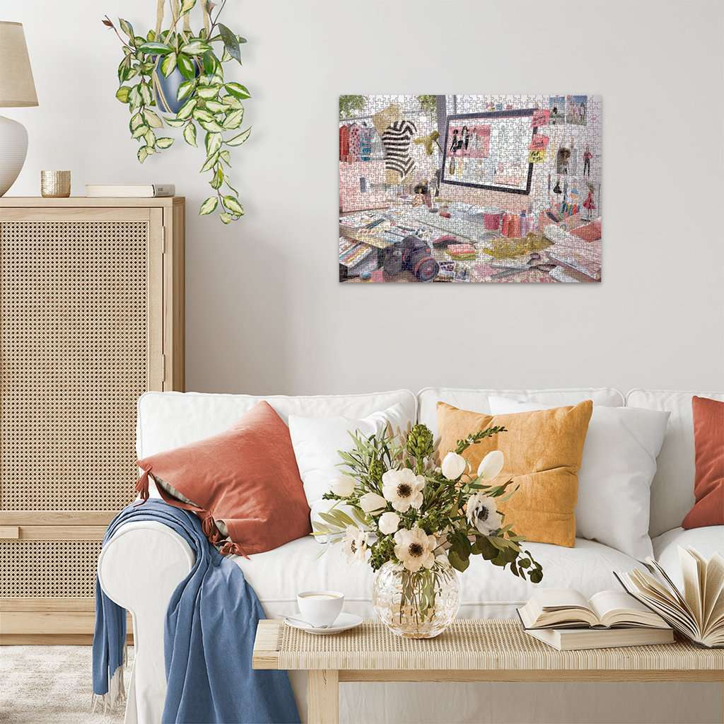 Ukończona układanka Barbie na białej ścianie, nad sofą i stołem z kwiatami i książkami.