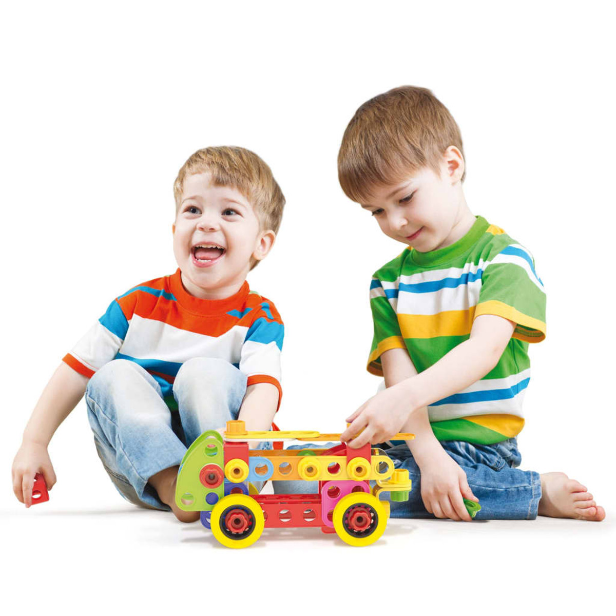 Dwóch małych chłopców bawiących się kolorową zabawką-ciężarówką. Jeden się śmieje. Białe tło.
