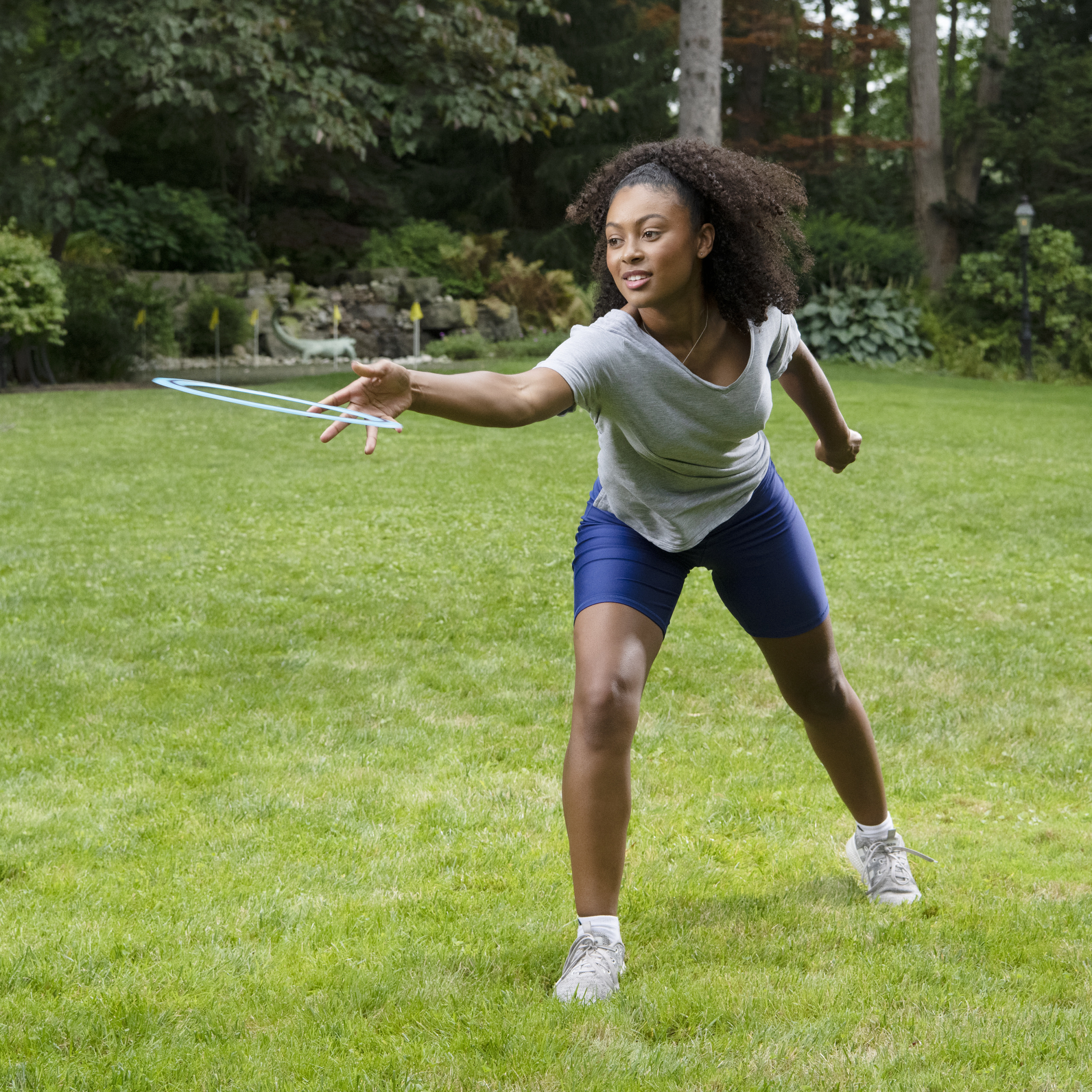 Kobieta rzuca niebieski pierścień na trawiastym podwórku. W tle drzewa.