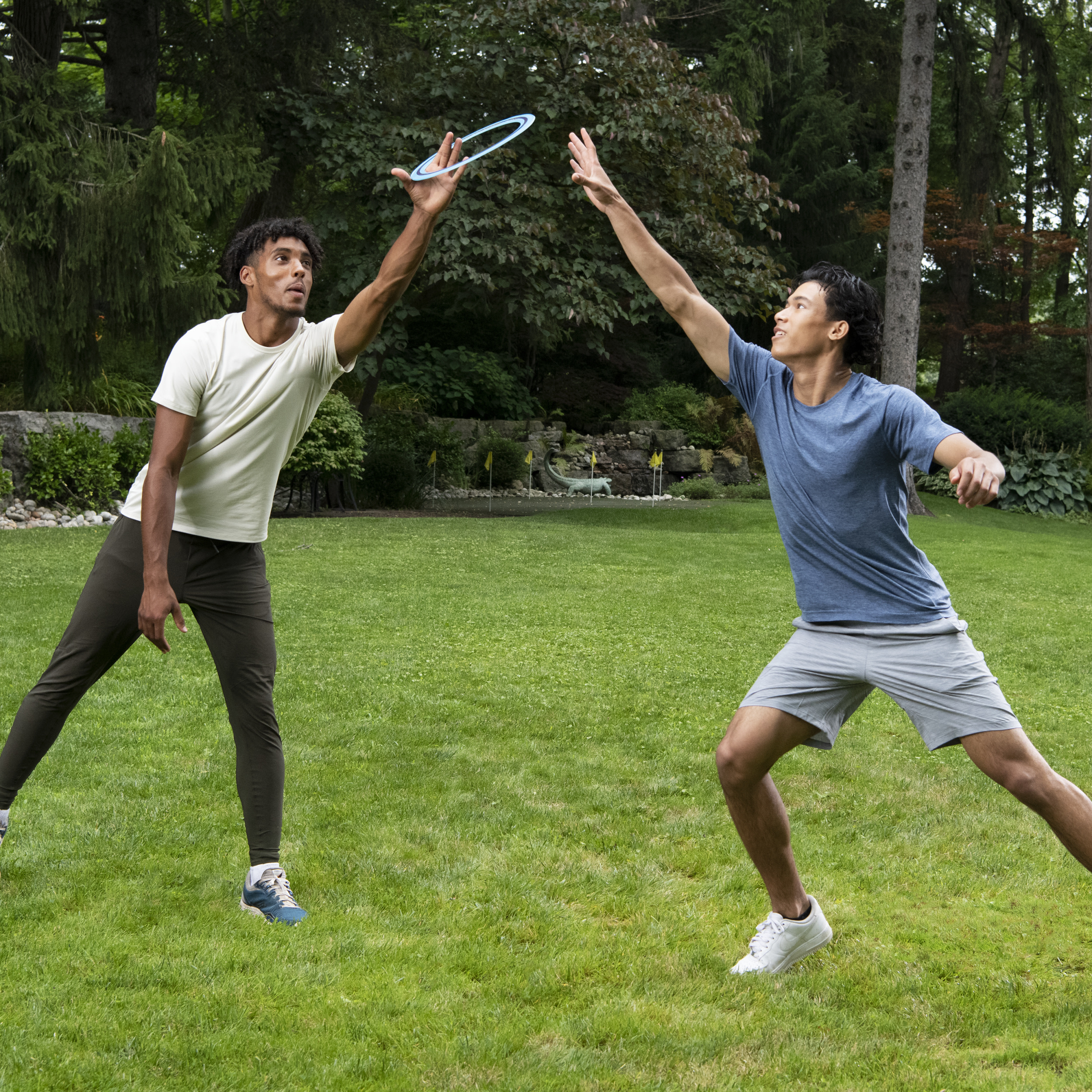Dwóch mężczyzn gra w frisbee na zielonym, trawiastym podwórzu. Jeden rzuca frisbee do drugiego.