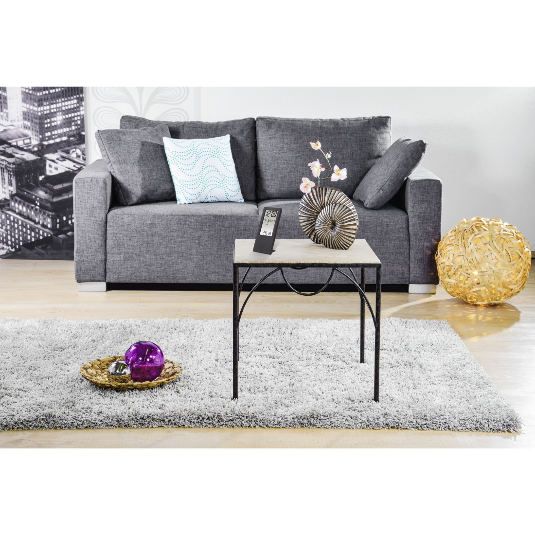 Scena w salonie z szarą sofą, stolikiem kawowym, dywanem i elementami dekoracyjnymi. W tle widok na miasto.