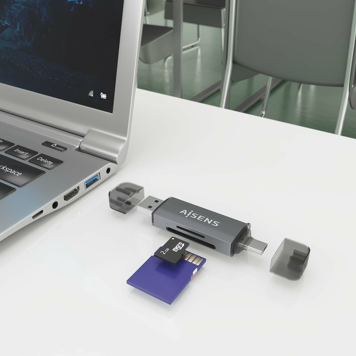 Laptop, szary czytnik kart i niebieska karta SD na białym biurku. Krzesła w tle.