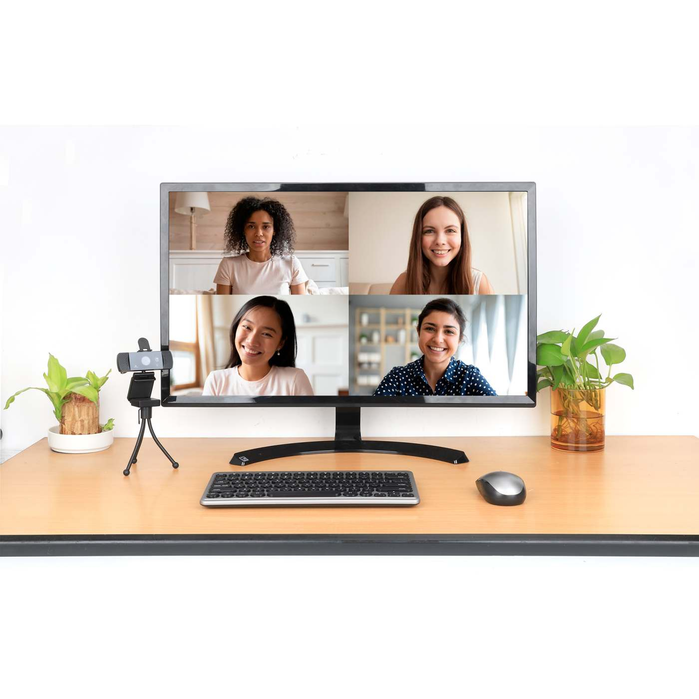 Un monitor di computer che mostra una videochiamata con quattro persone. Una webcam e una tastiera sono sulla scrivania.