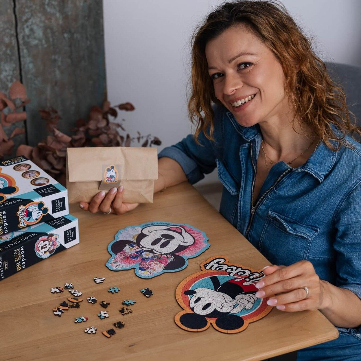 Woman with jigsaw puzzles on a wooden table, smiling. Puzzles with Disney characters.